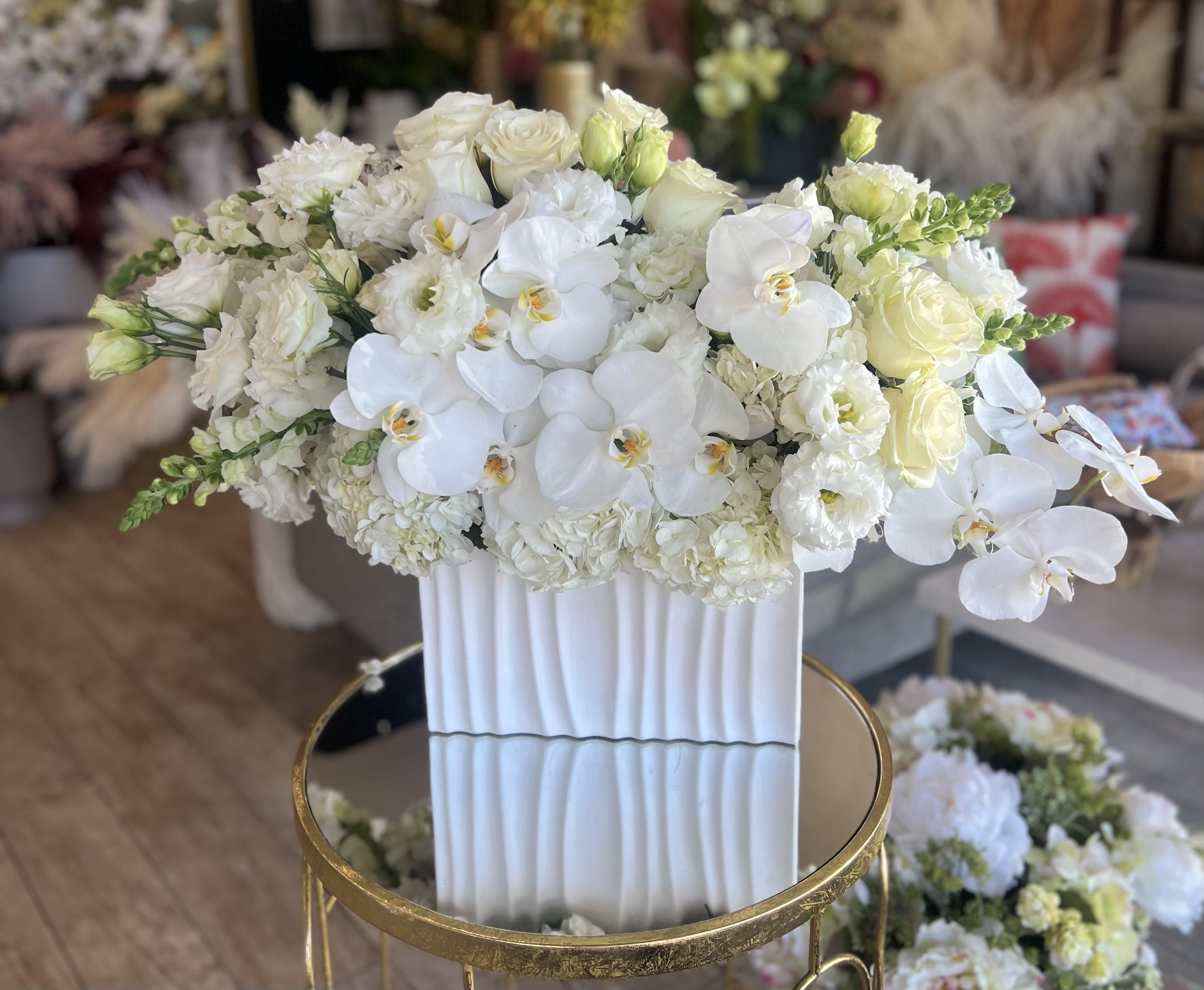 White floral arrangement in a tall ribbed vase with orchids and roses