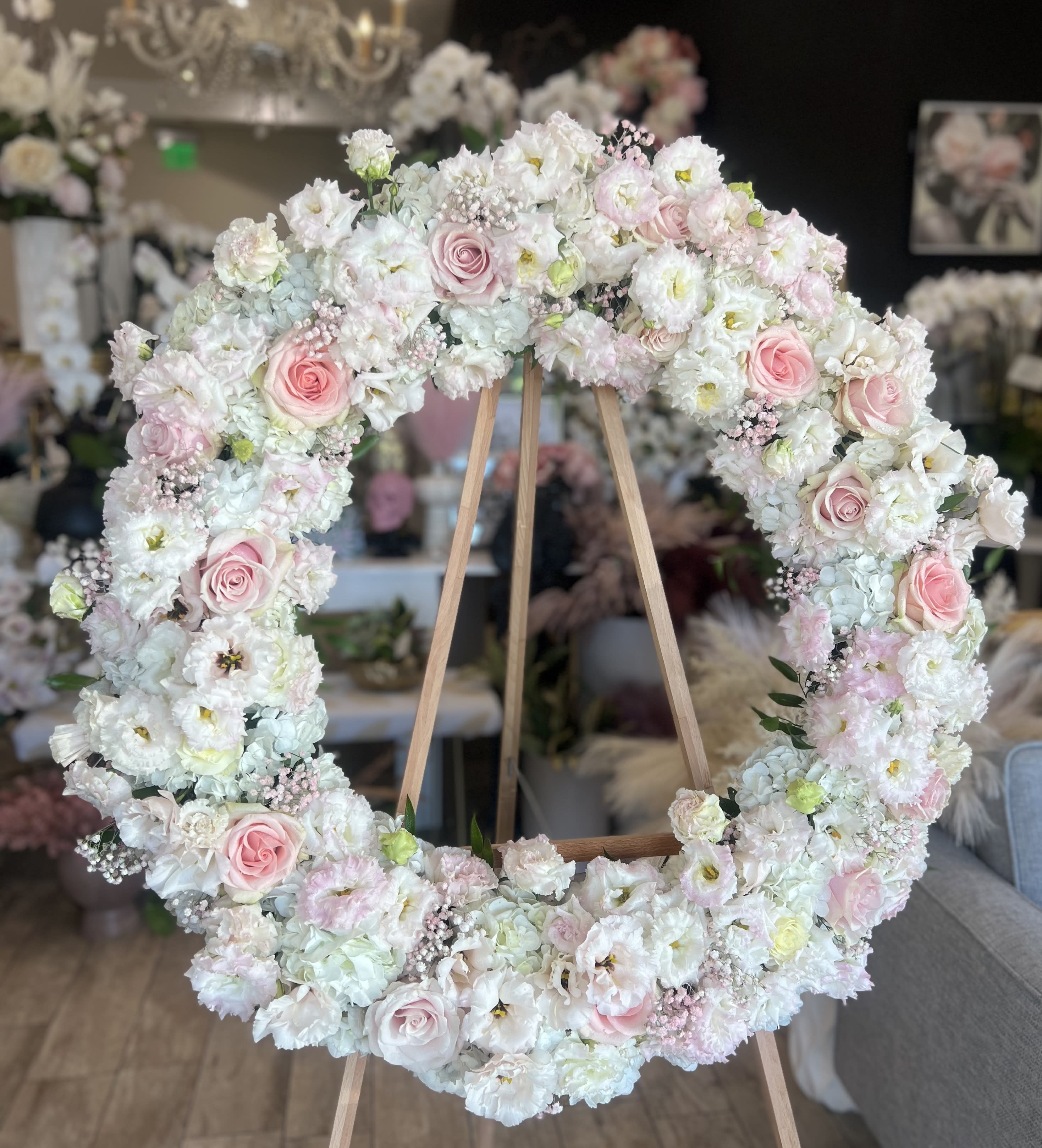 Large pastel floral wreath on a wooden easel with pink roses and white blooms