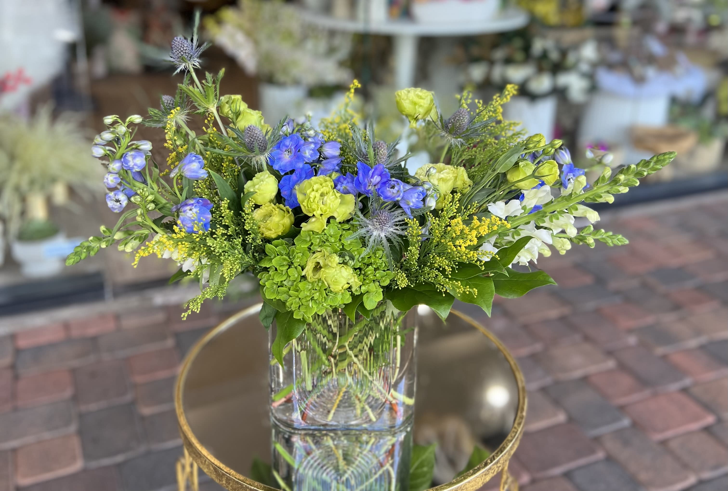 Mixed bouquet of blue, green, and white flowers in a clear glass vase