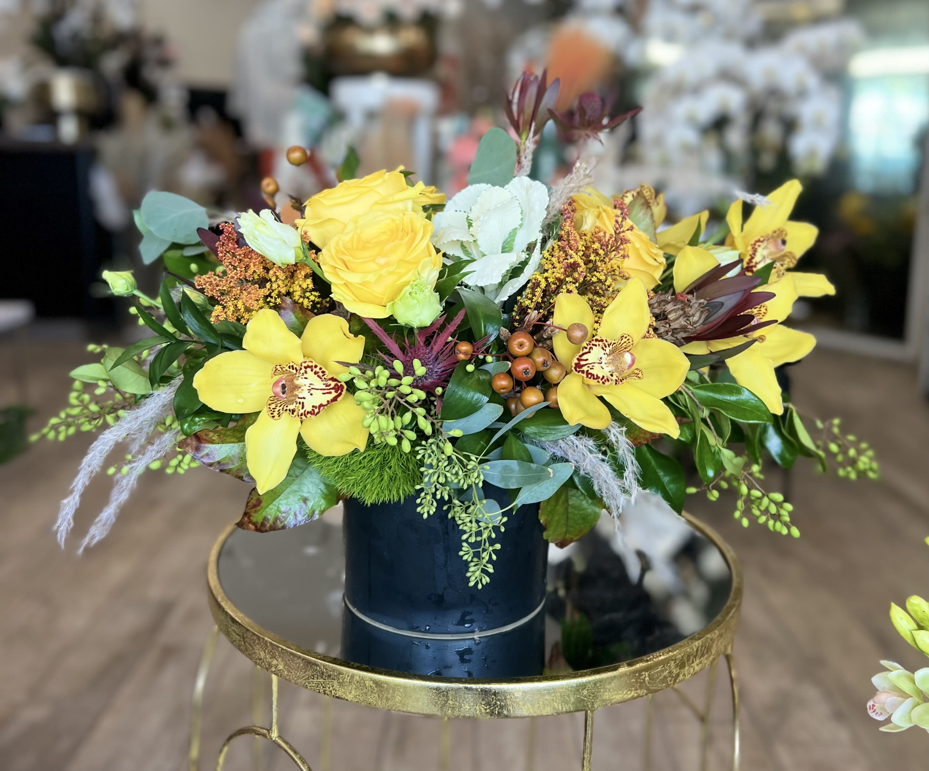 Yellow roses and orchids arranged in a dark vase