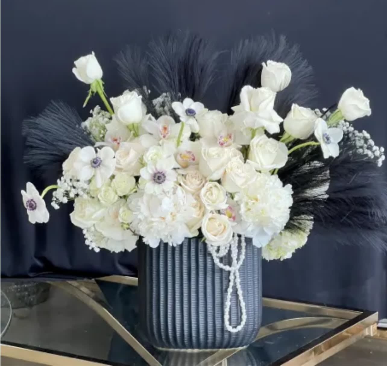 White floral arrangement in a ribbed blue vase with dark feather accents