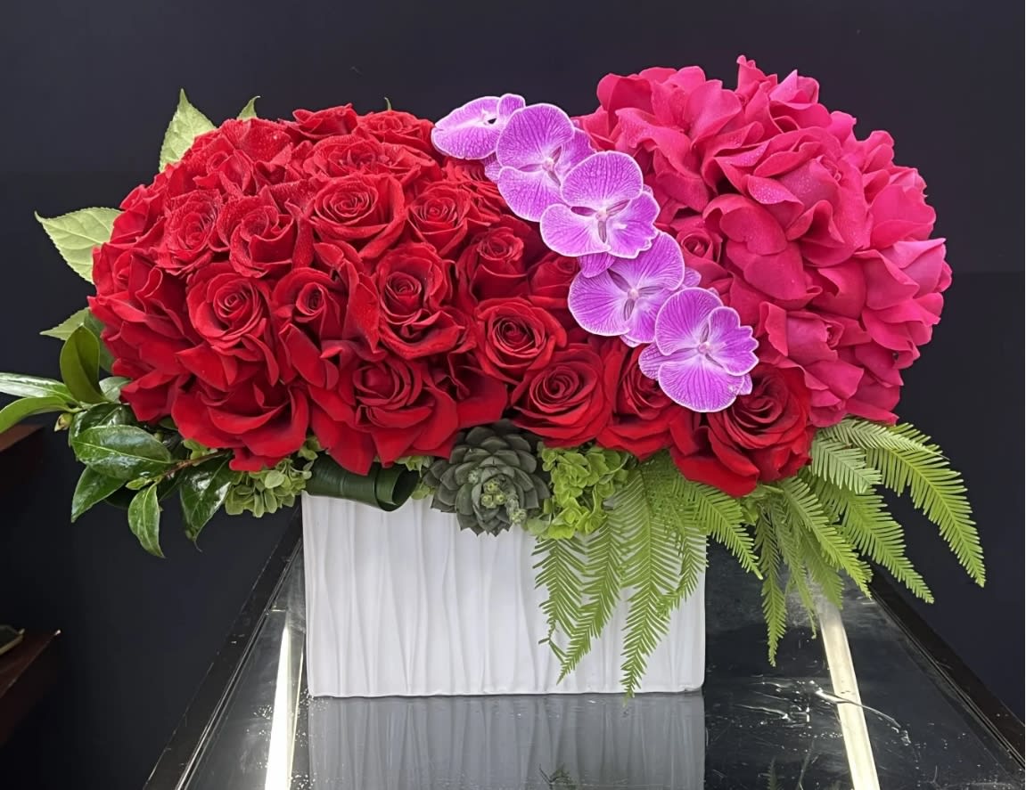 Red roses and pink hydrangeas with purple orchids in a white vase