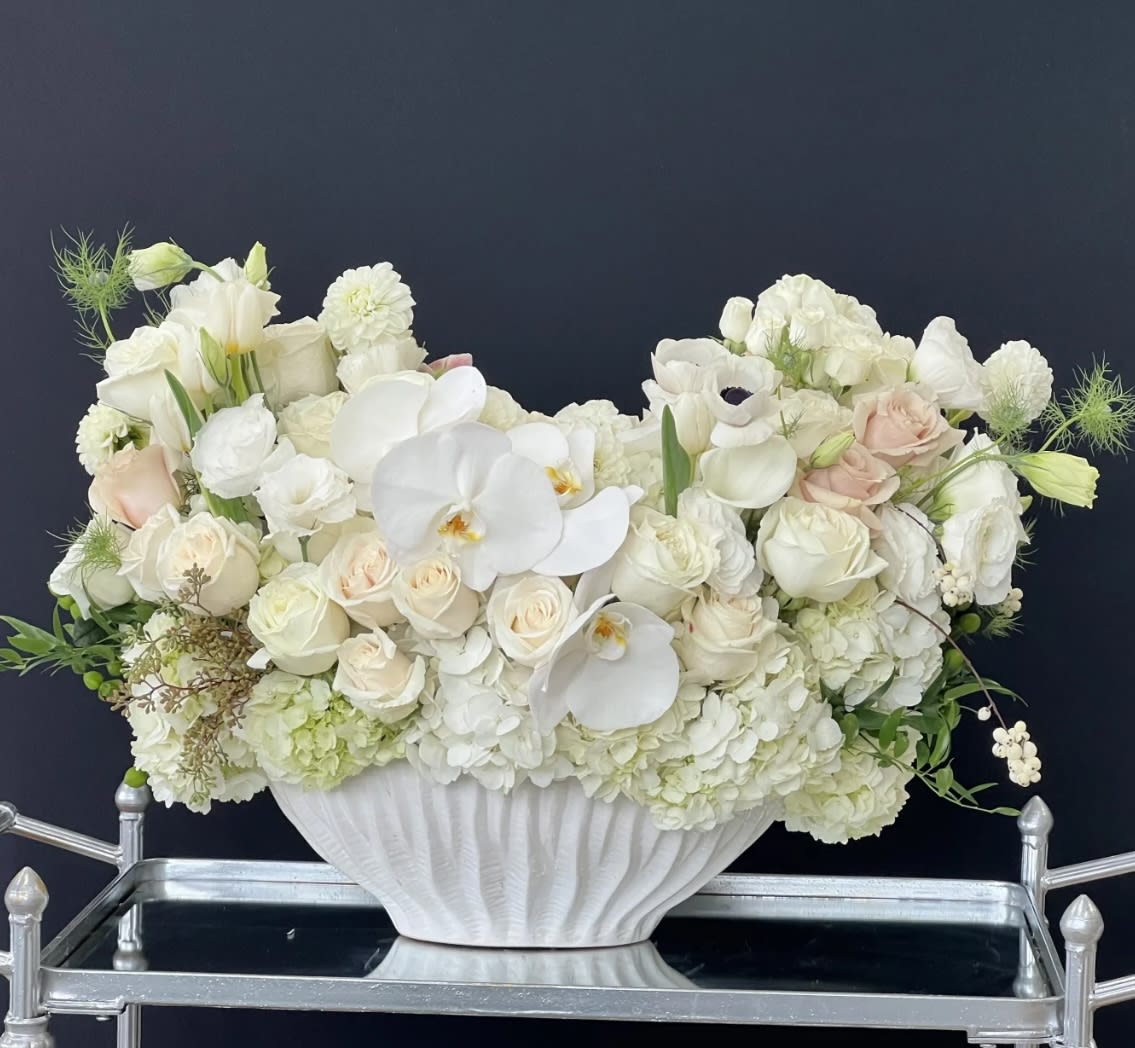 White floral arrangement in a white pedestal vase with pale blush roses and orchids