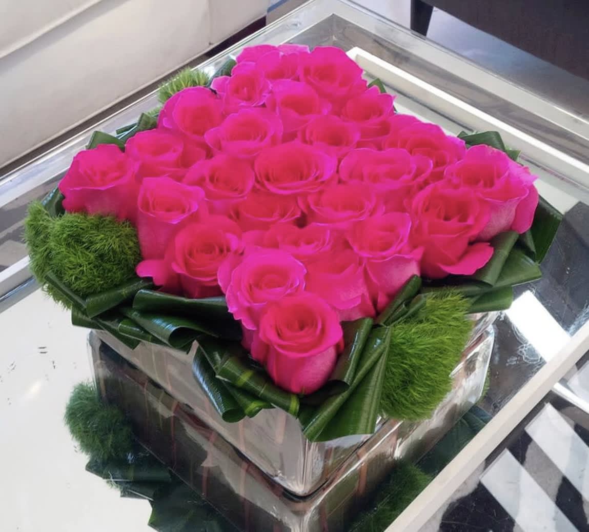 Hot pink roses arranged in a square glass box with green accents