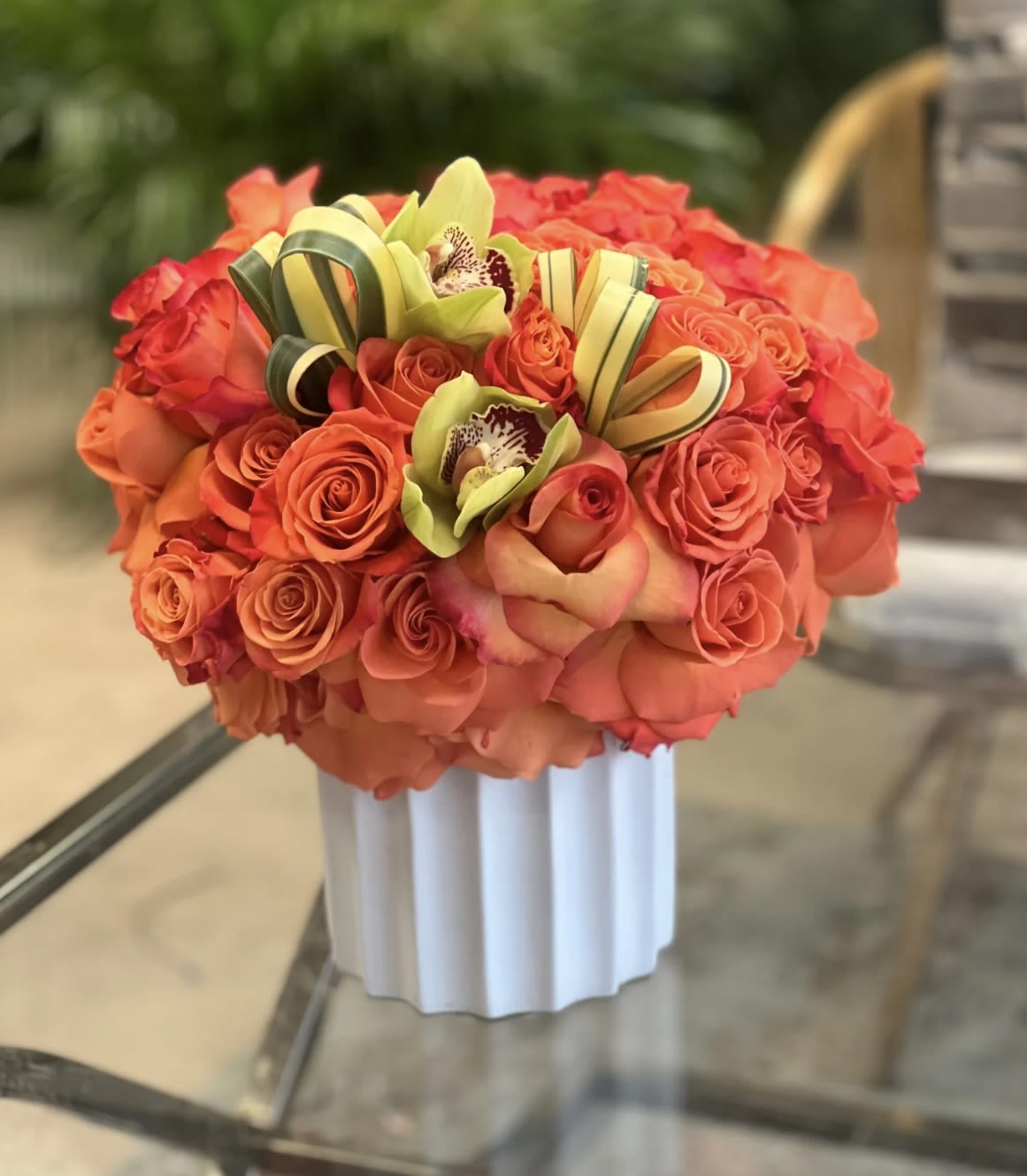 Orange rose bouquet with green orchids in a white vase