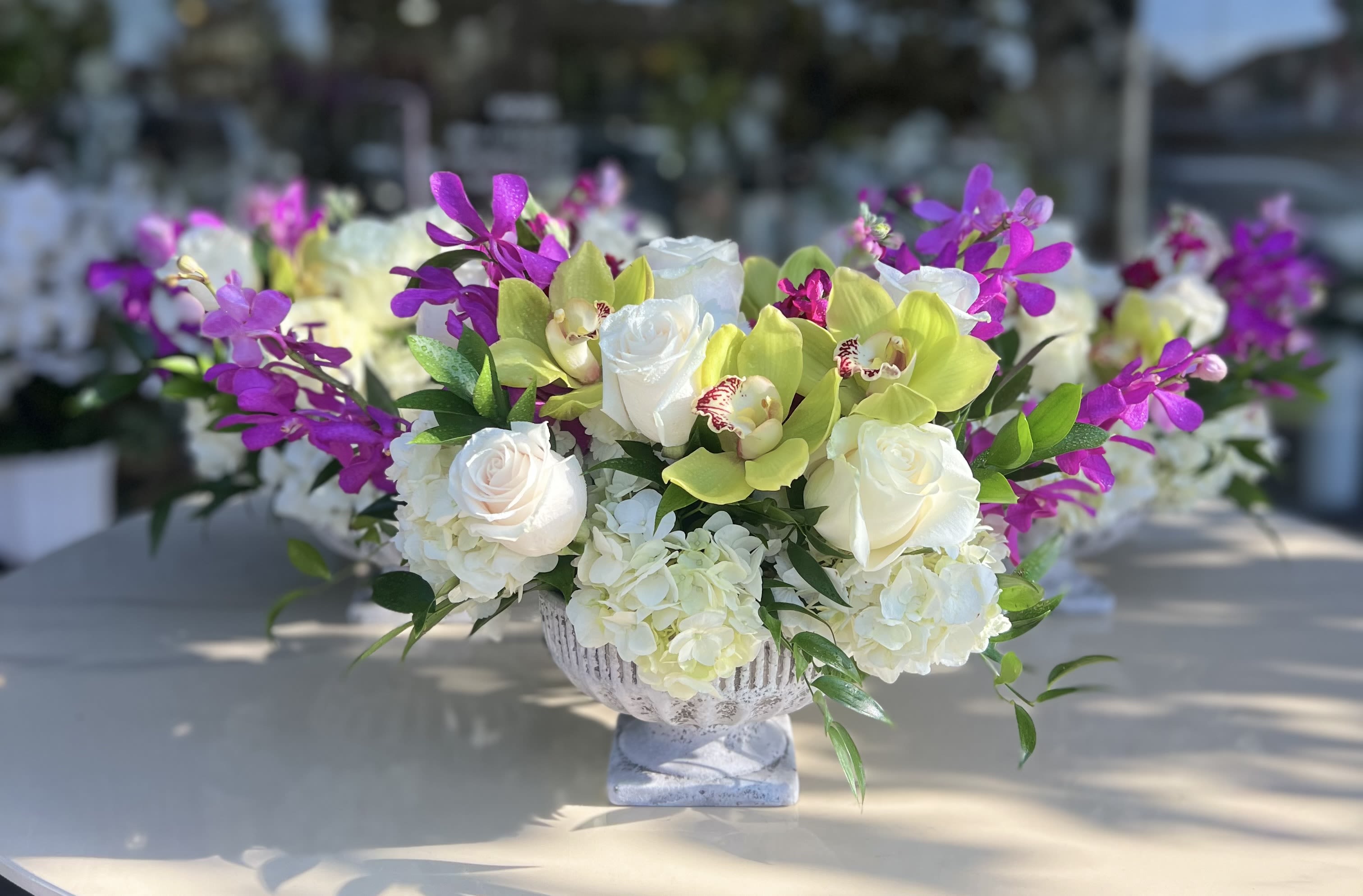 White roses and hydrangeas with purple orchids in a pedestal vase