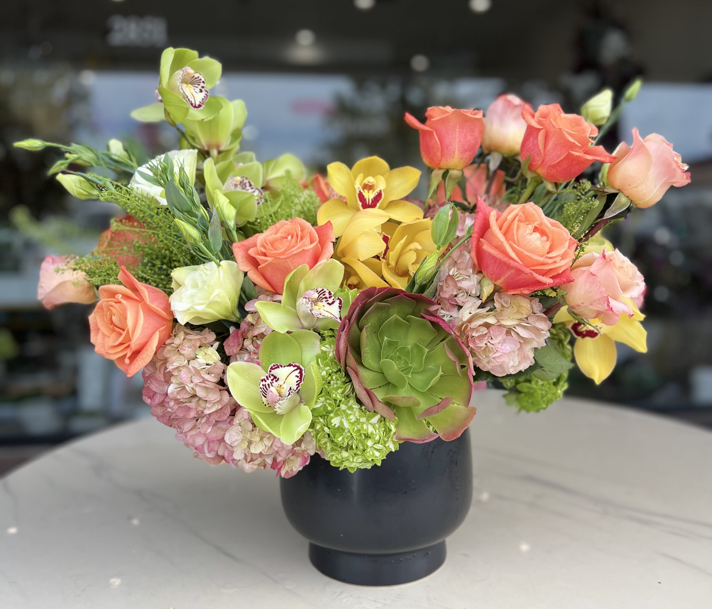 Mixed bouquet with roses, orchids, hydrangeas, and a succulent in a black vase