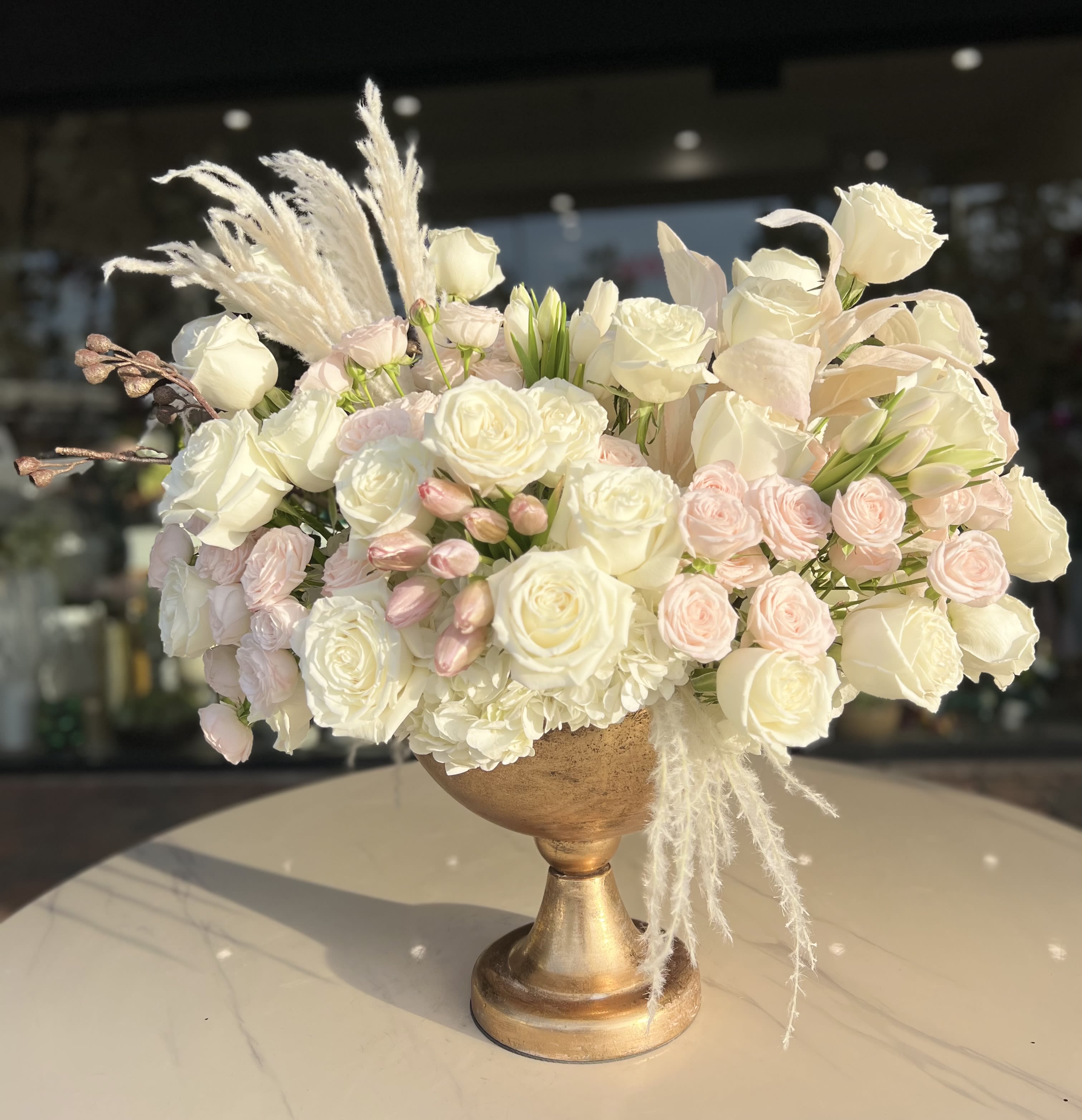 Cream and blush rose arrangement in a gold pedestal vase