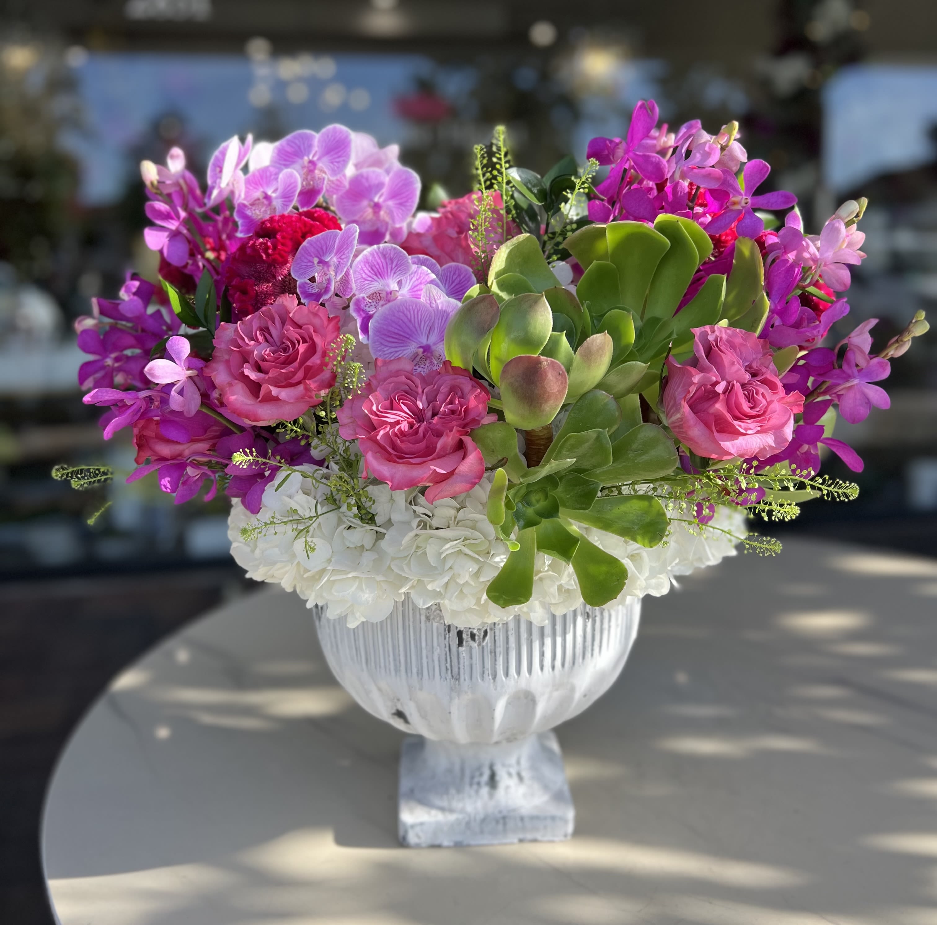 Pink orchids and roses arranged in a white pedestal vase
