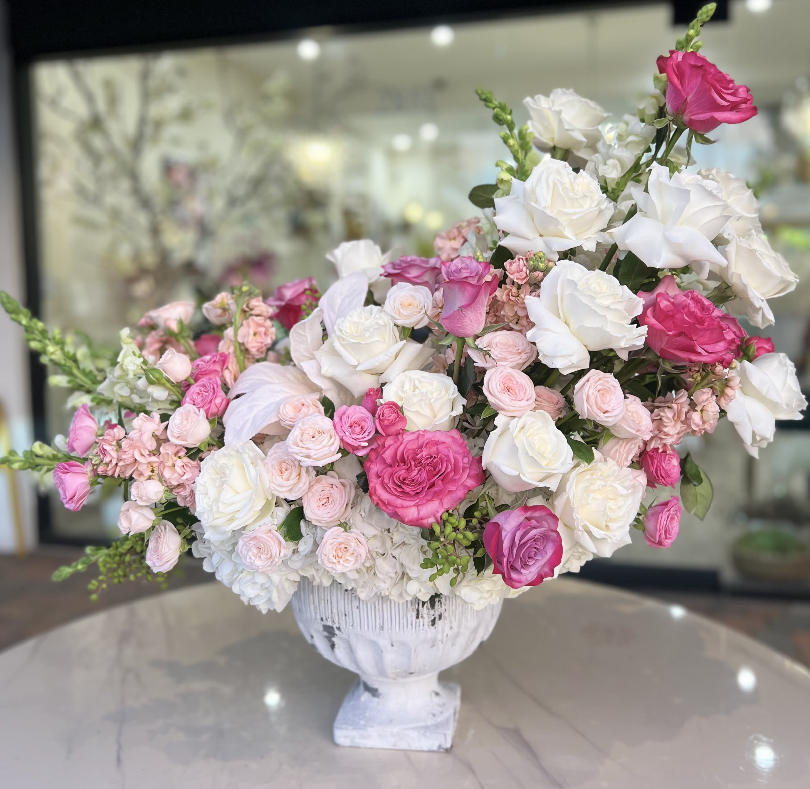 Pink and white rose arrangement in a white pedestal vase