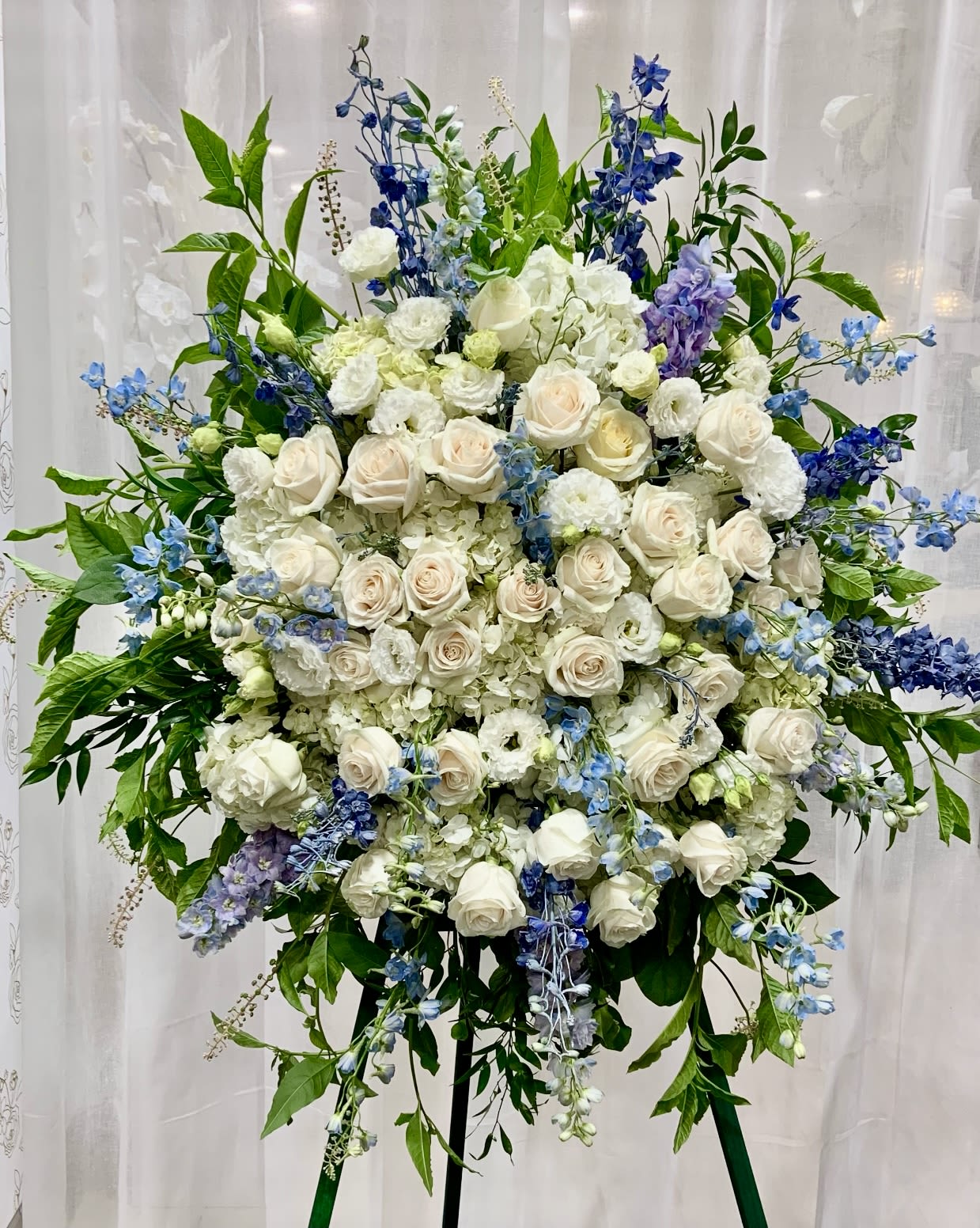 Large standing floral spray with white roses and blue flowers on an easel
