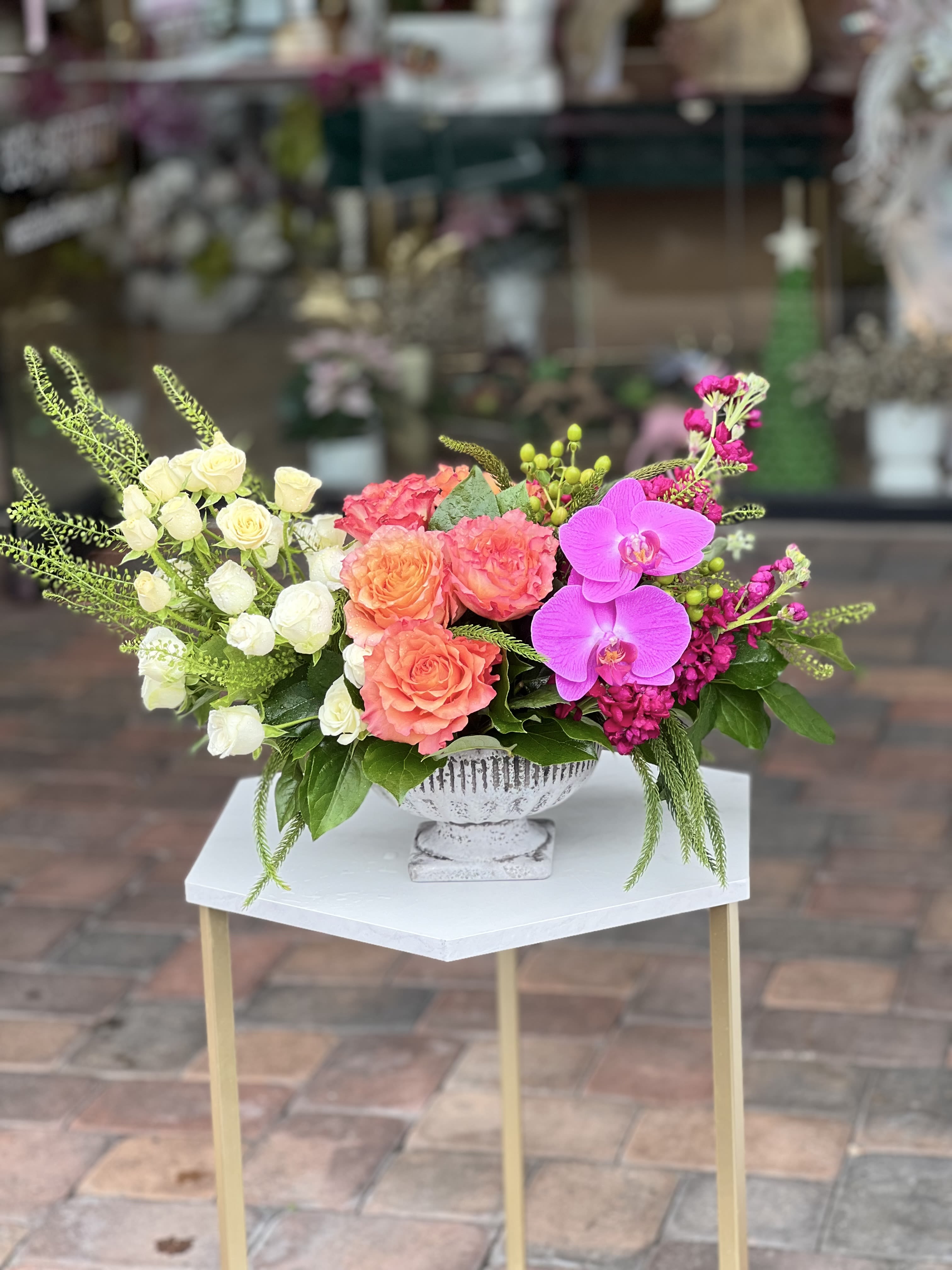 Mixed floral arrangement with roses, orchids, and pink blooms in a white pedestal vase