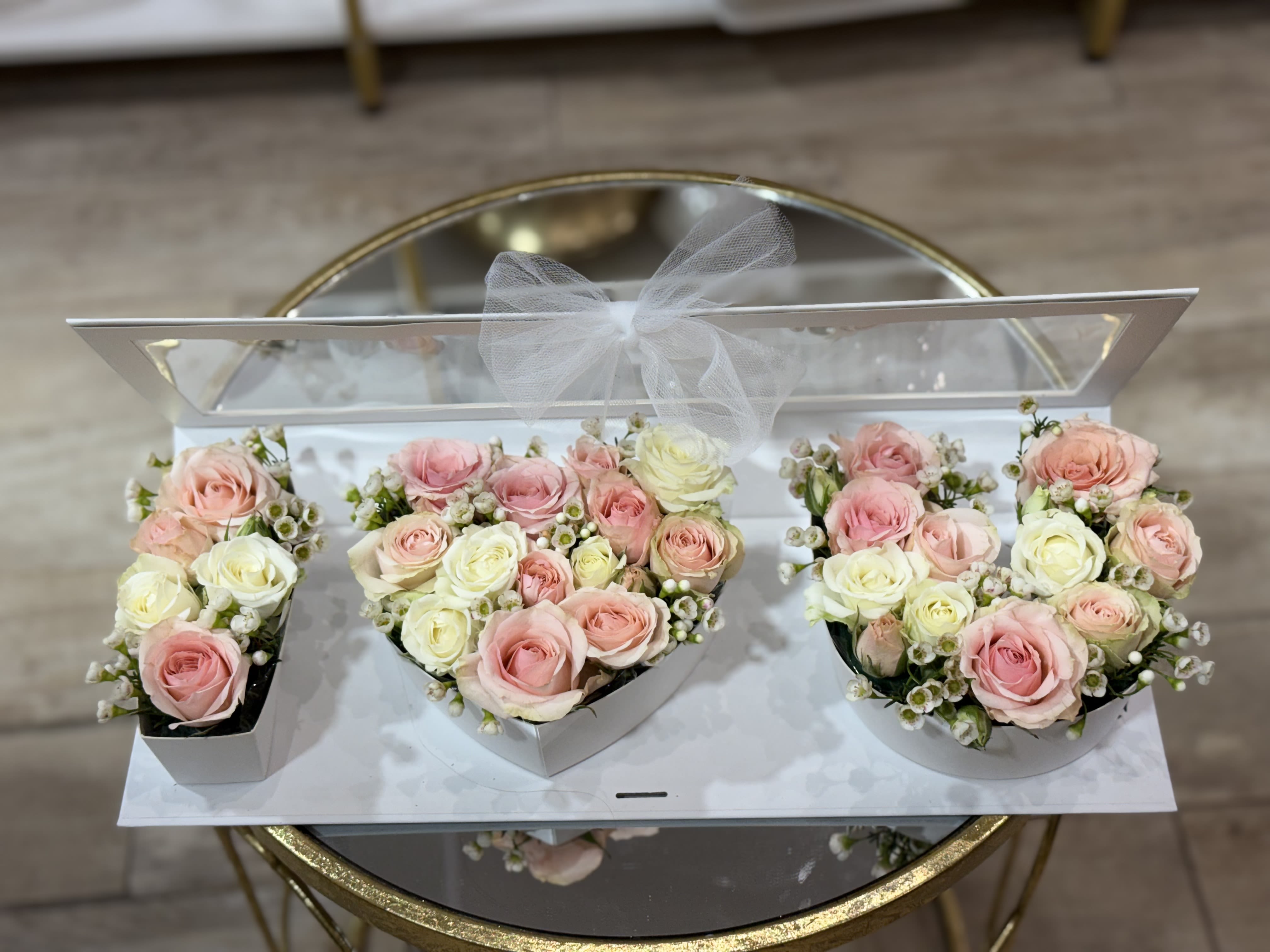 Three pastel rose arrangements in white boxes with a sheer bow