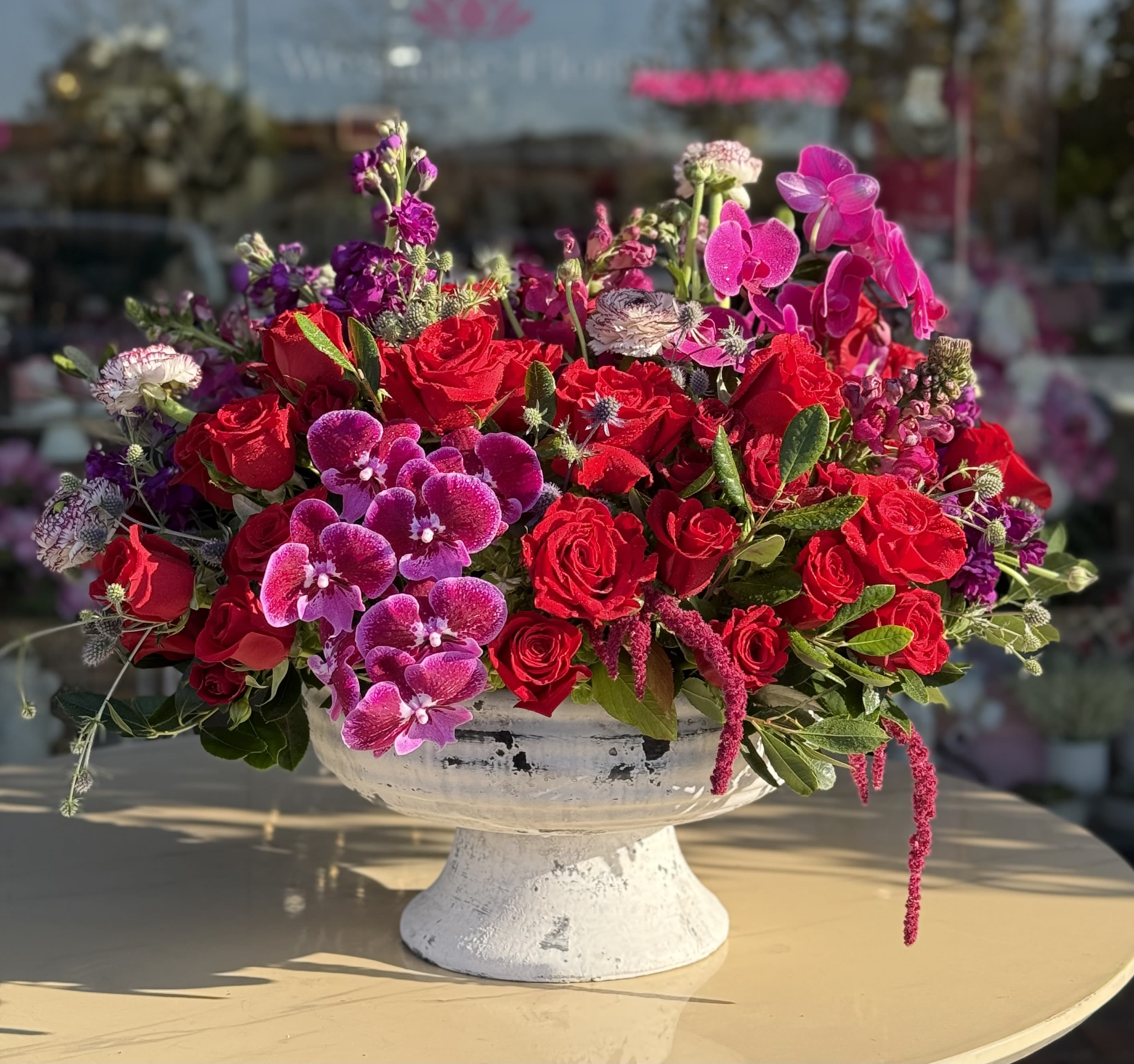 Red roses and pink orchids in a white pedestal bowl