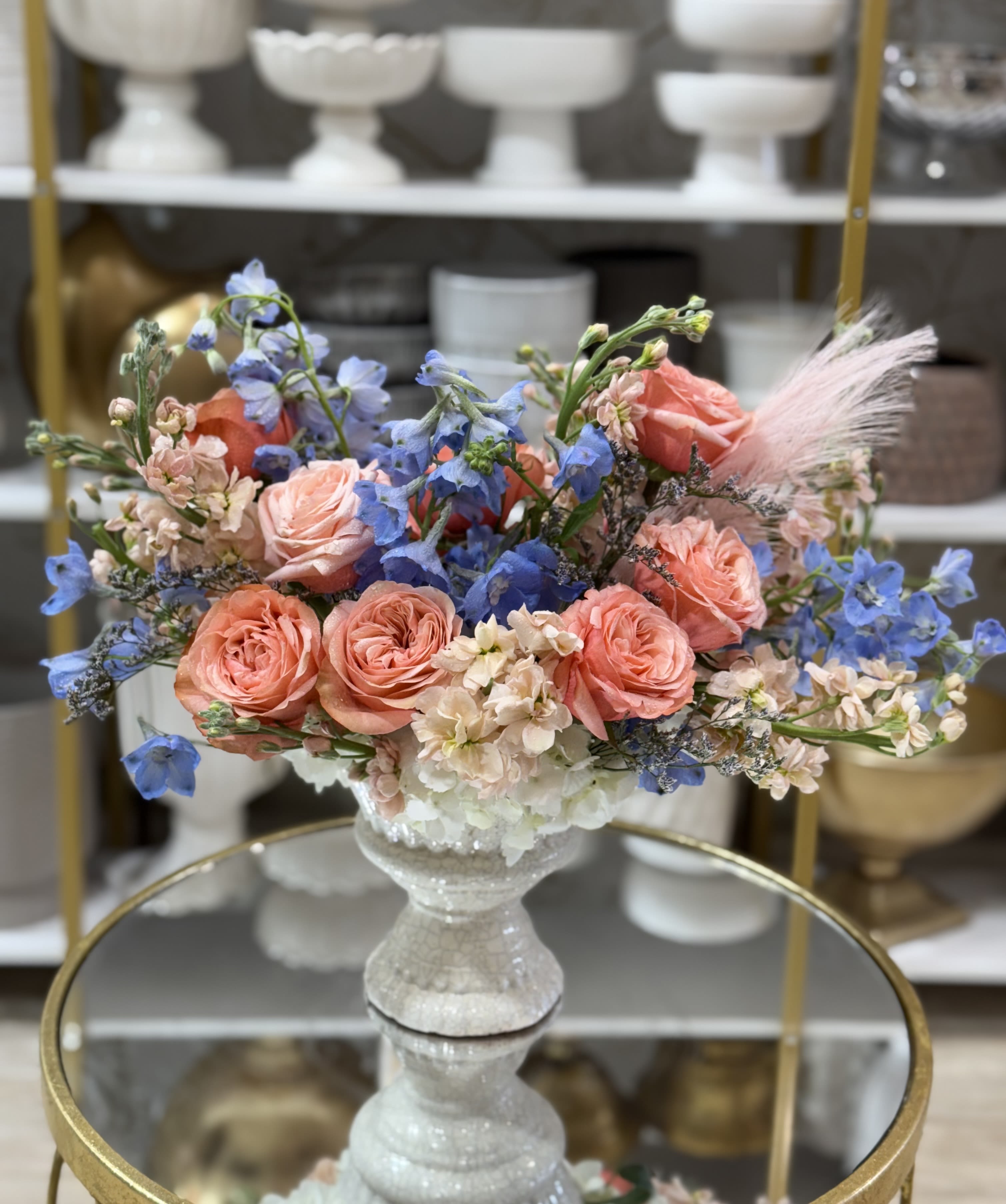 Bouquet of peach roses and blue flowers in a white pedestal vase