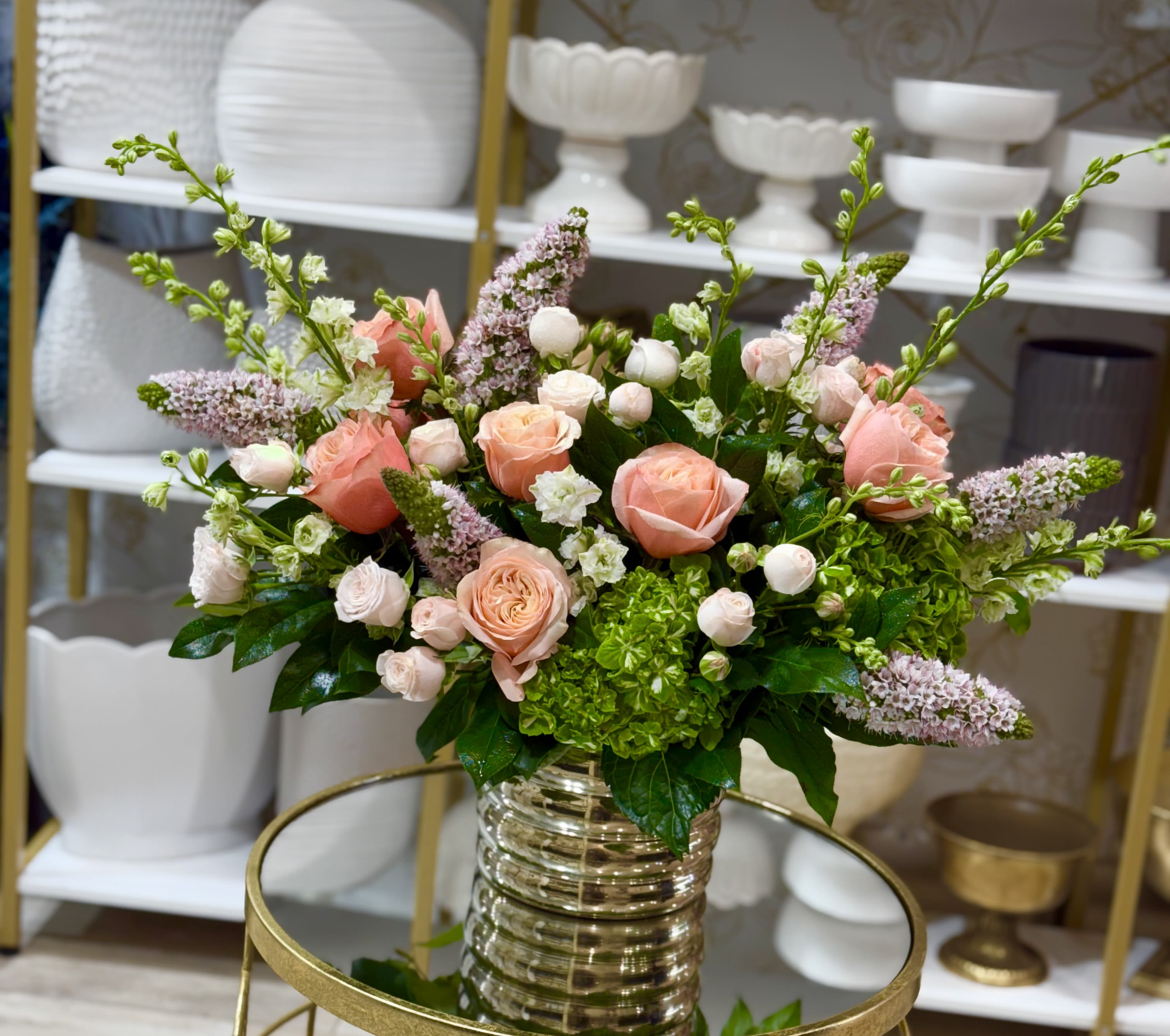 Peach and blush roses in a clear ribbed vase with green hydrangea and lilac spikes