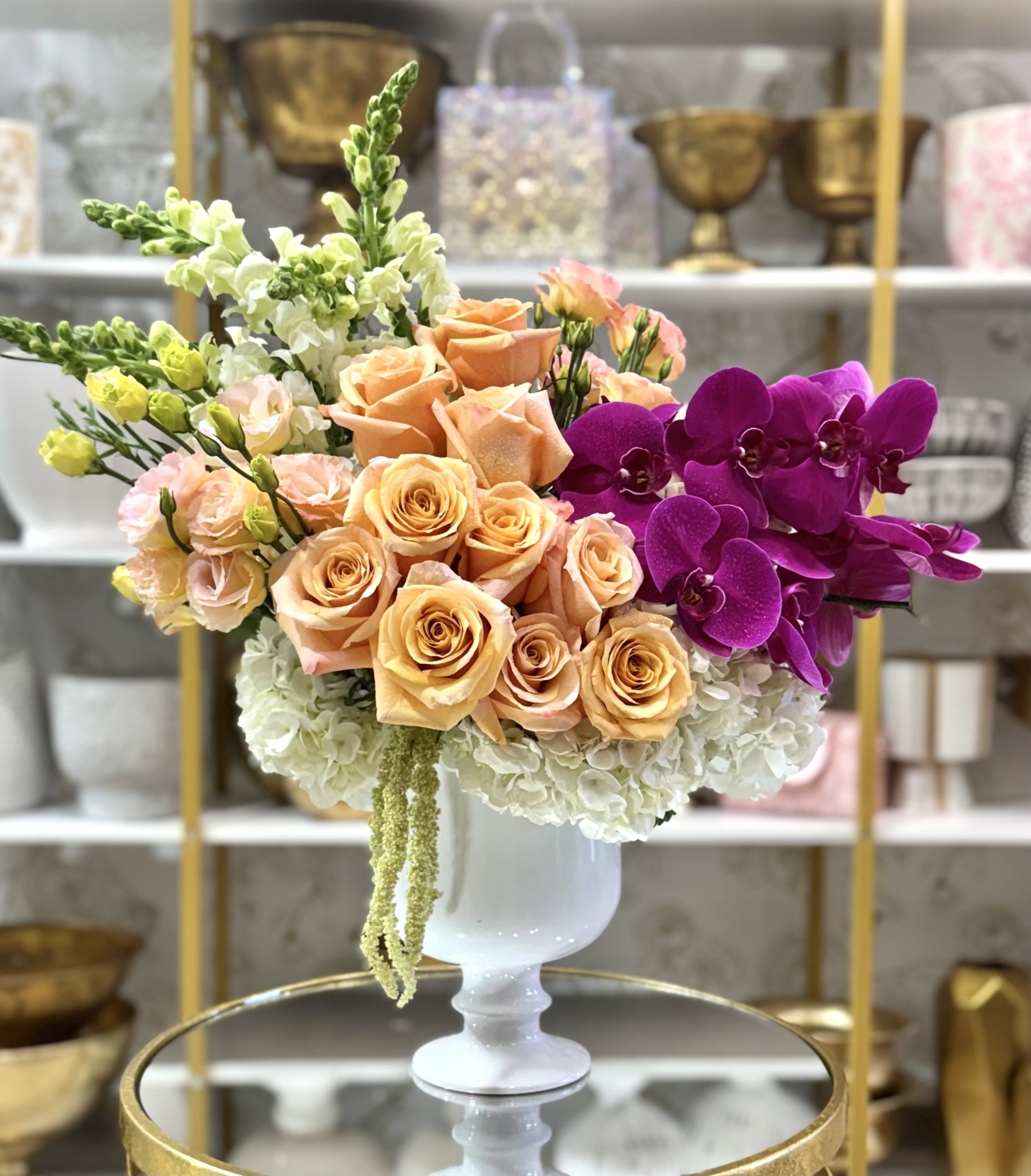 Peach roses and purple orchids in a white pedestal vase