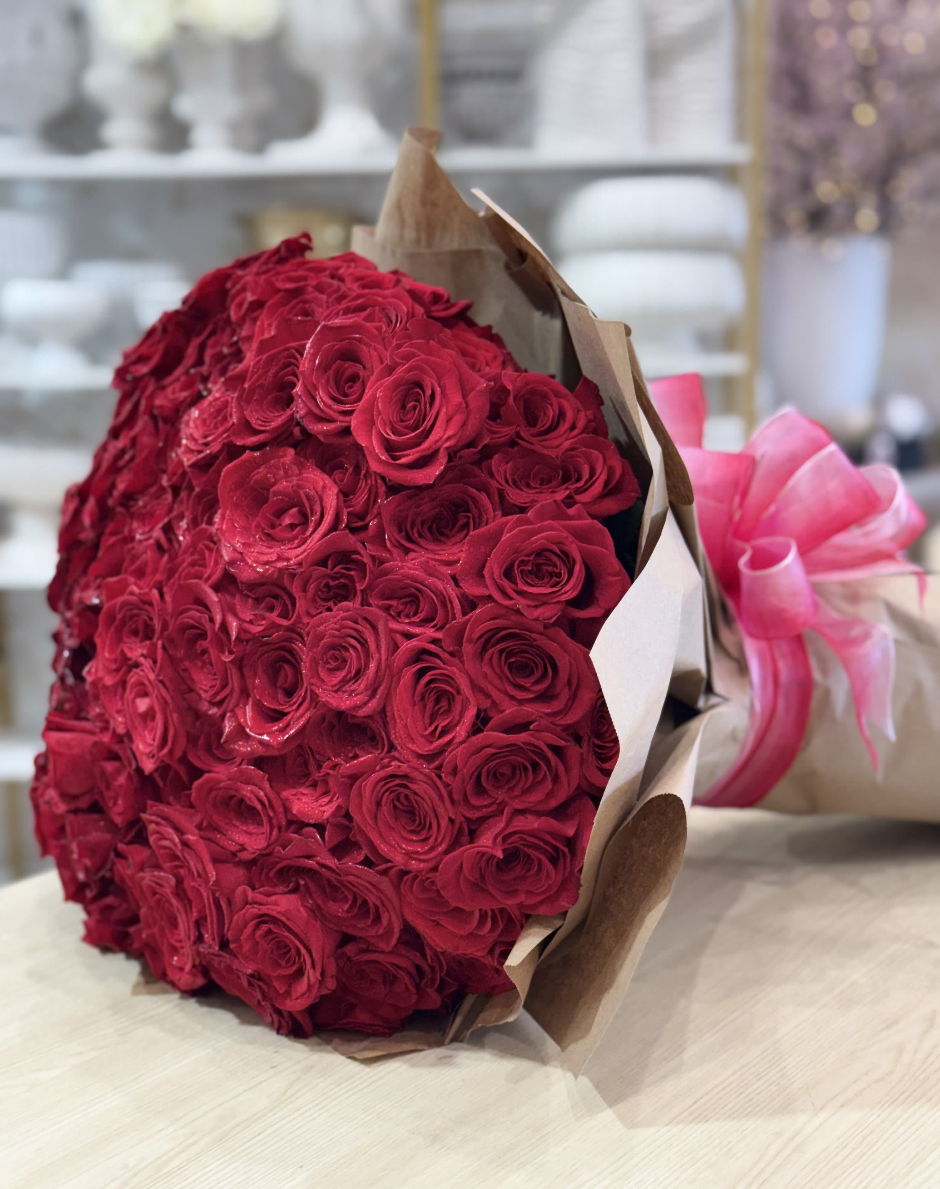 Large bouquet of red roses wrapped in brown paper with a pink ribbon