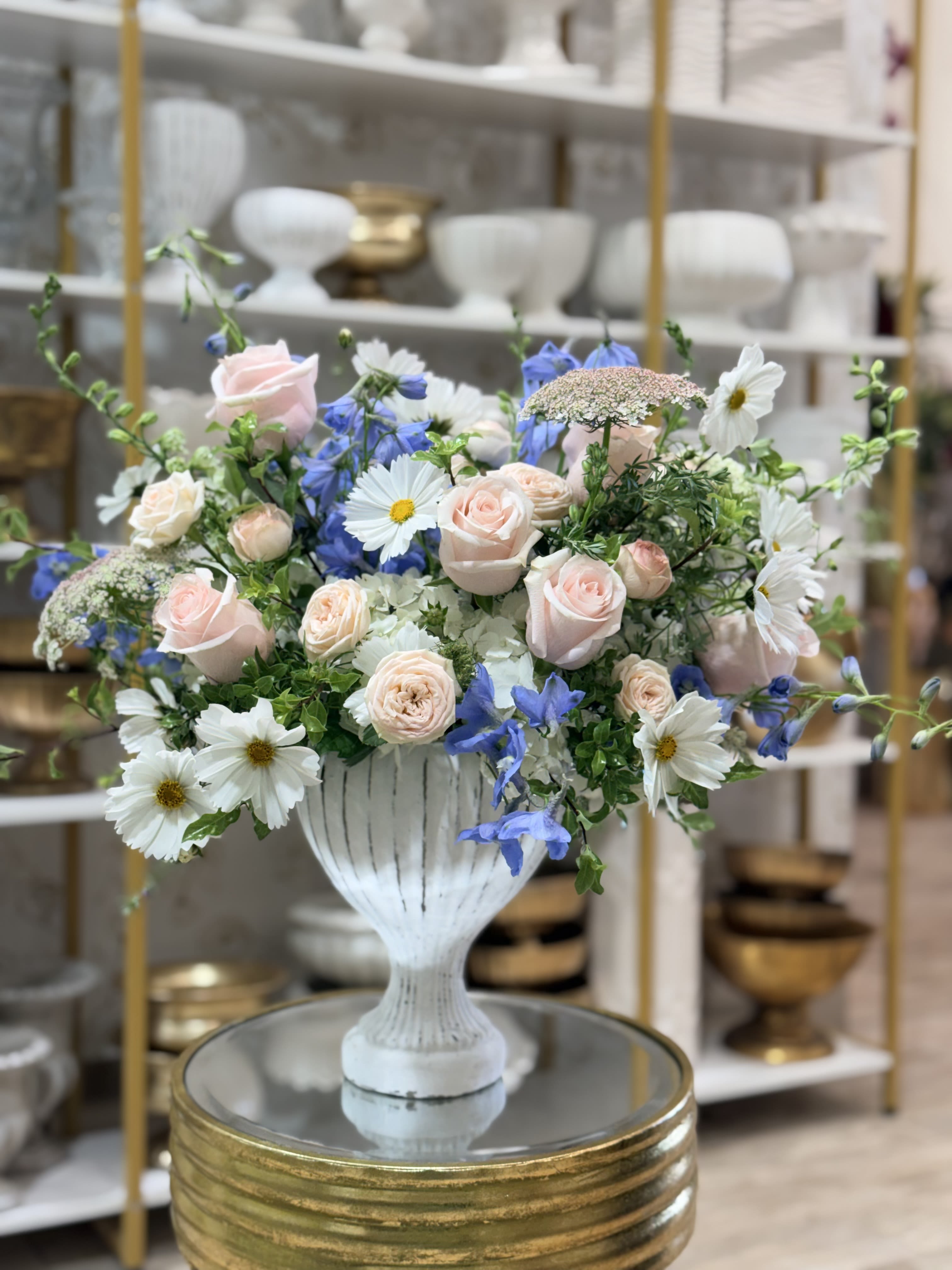 Pastel bouquet of pink roses, white daisies, and blue flowers in a white vase