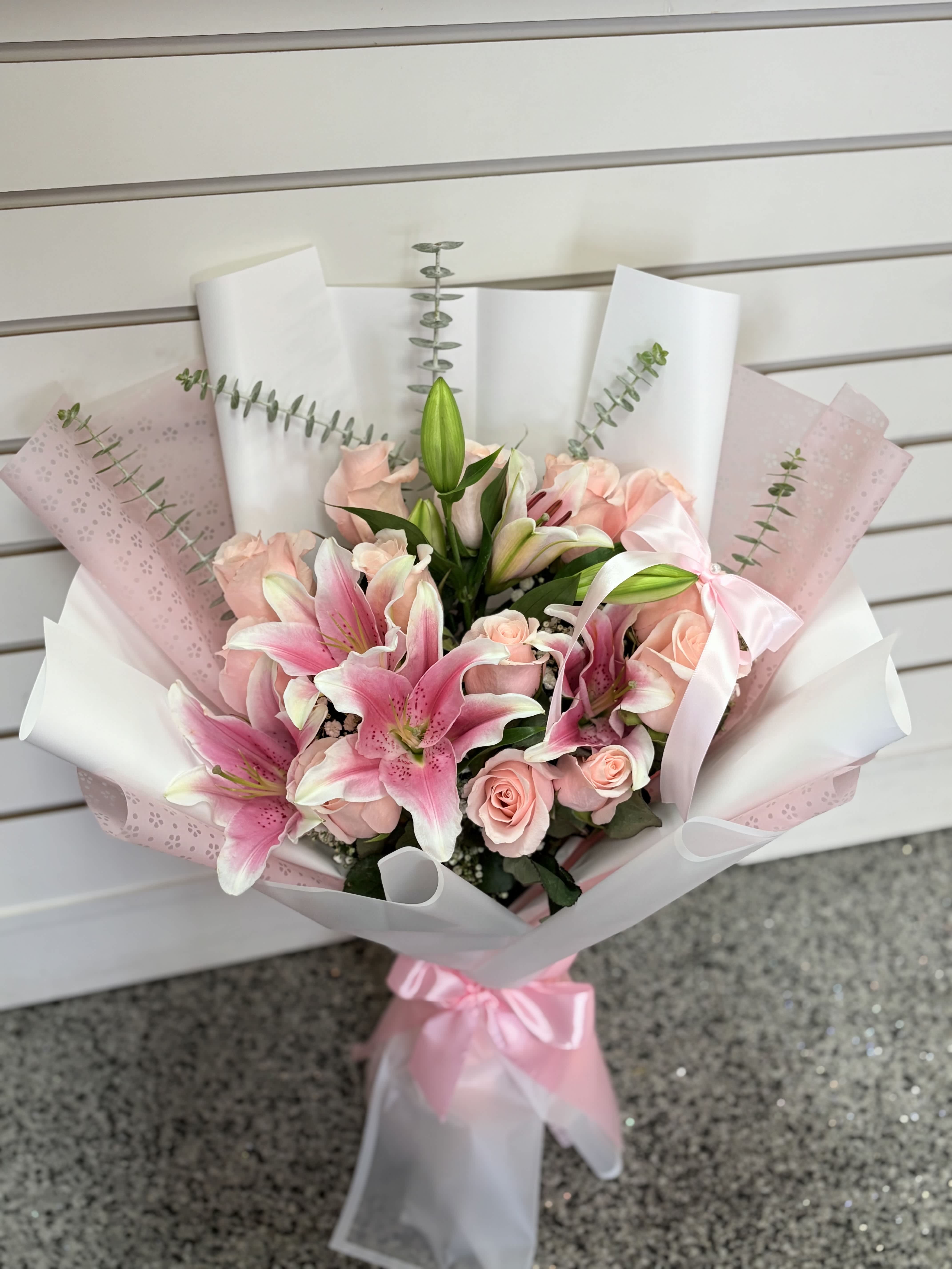 Pink lilies and roses wrapped in white and pink paper with a ribbon