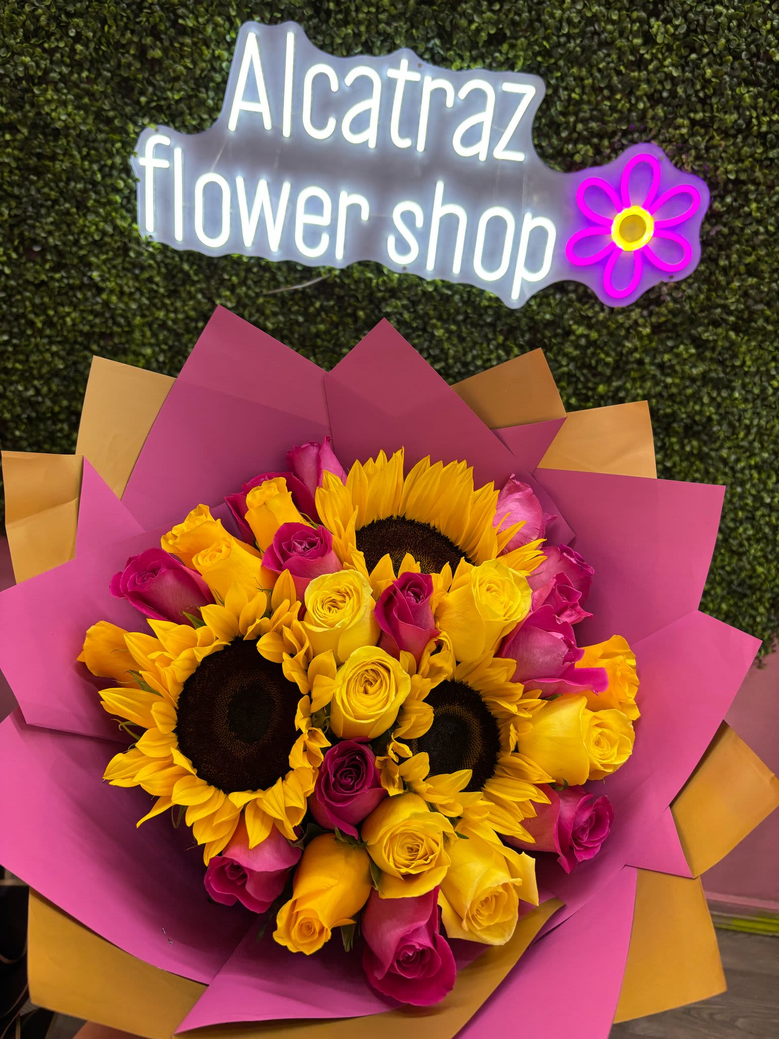 Bouquet of yellow sunflowers and pink and yellow roses wrapped in magenta paper