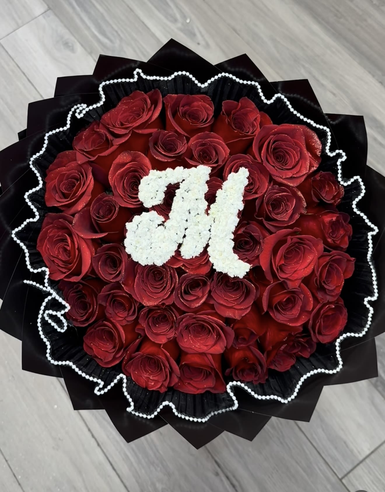 Round bouquet of red roses with a white floral monogram on black wrap