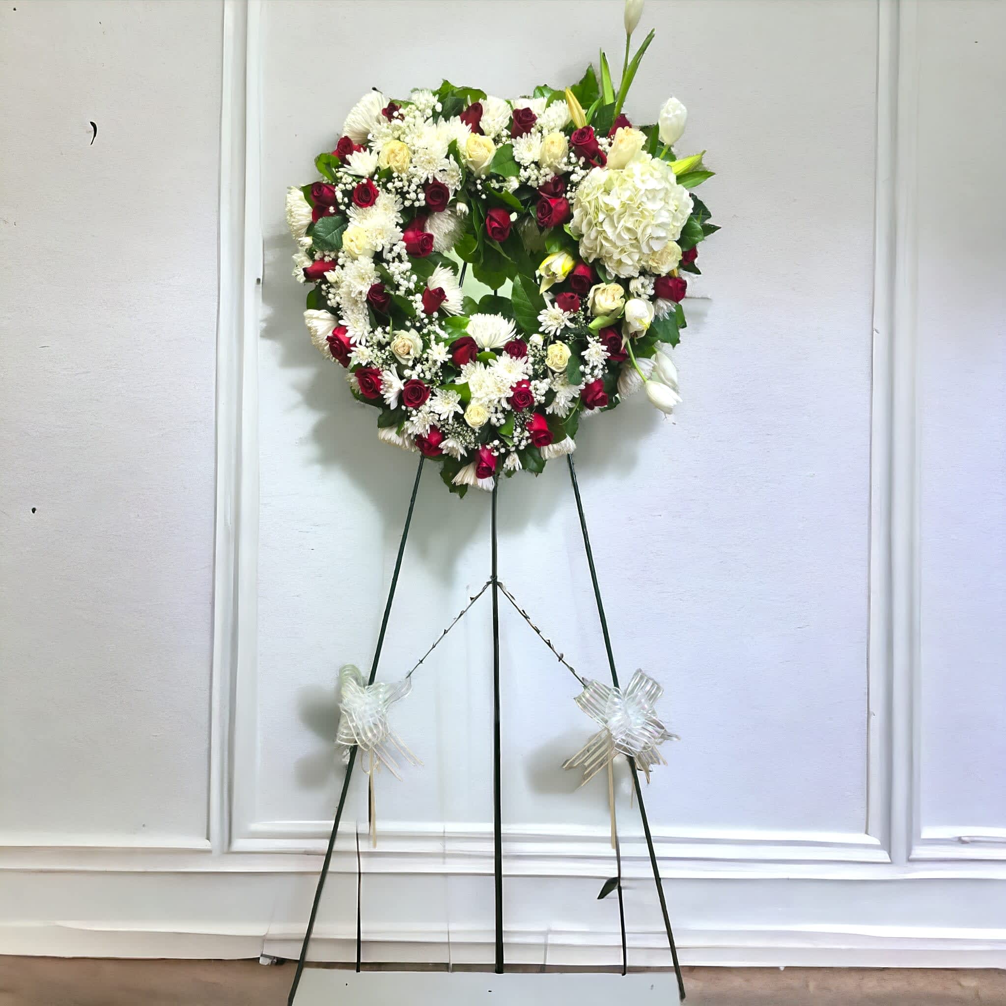 Heart-shaped floral wreath on a standing easel with red and white flowers