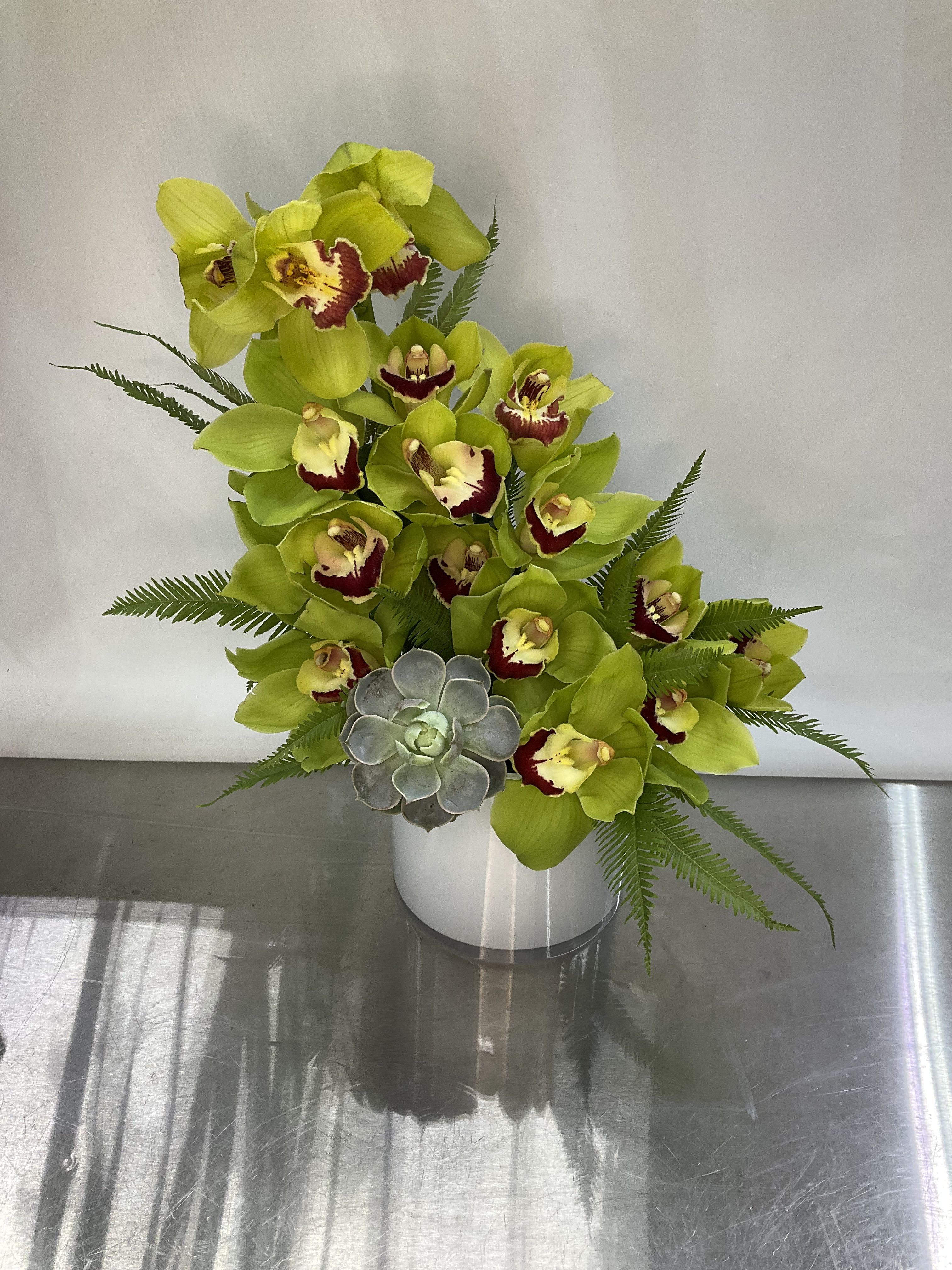 Green orchids arranged in a white vase with a small succulent accent