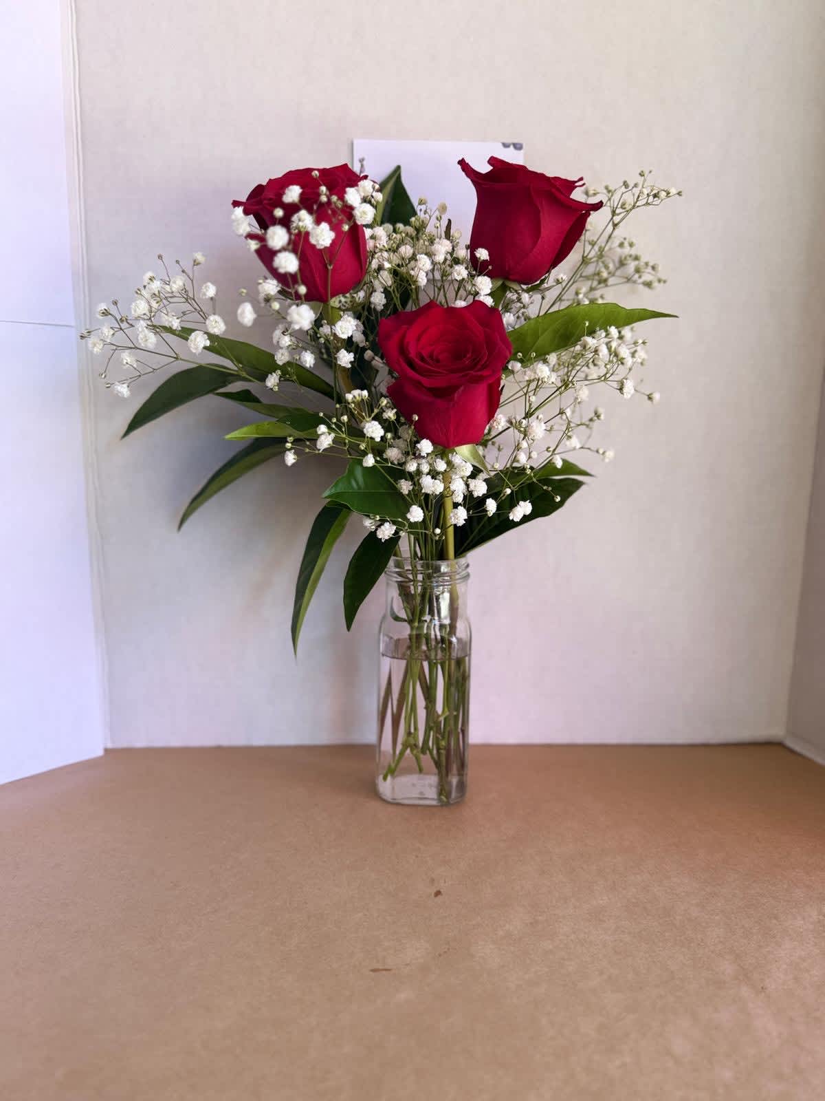 Three red roses in a clear glass vase with white baby's breath