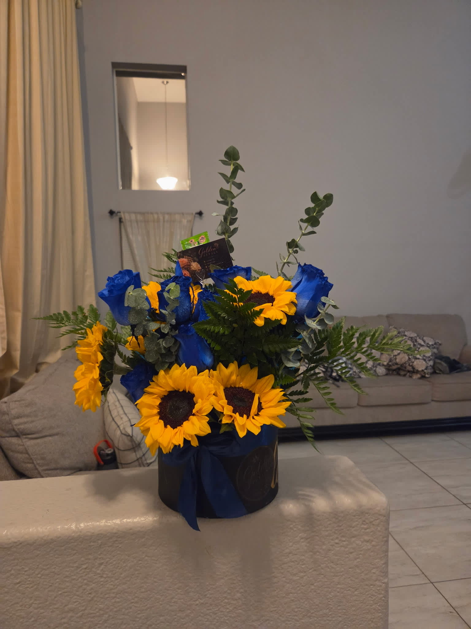 Blue roses and sunflowers arranged in a black hat box