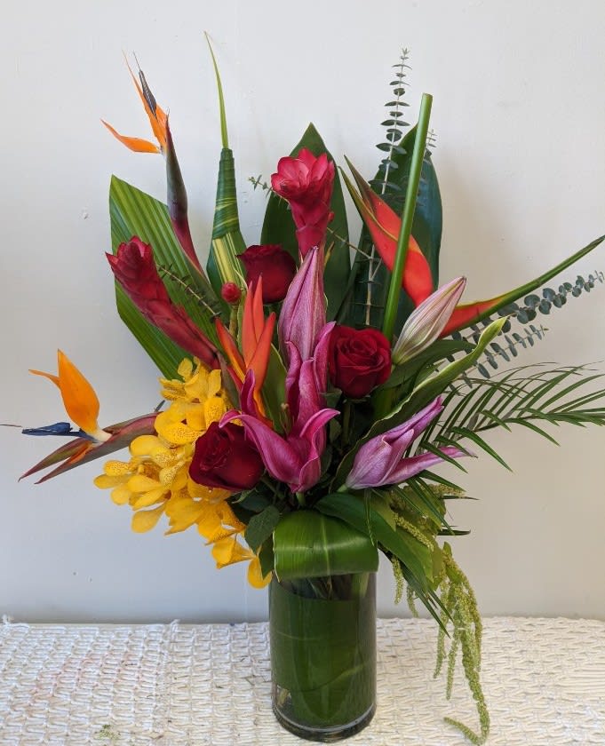 Tropical bouquet with red roses and orchids in a tall glass vase