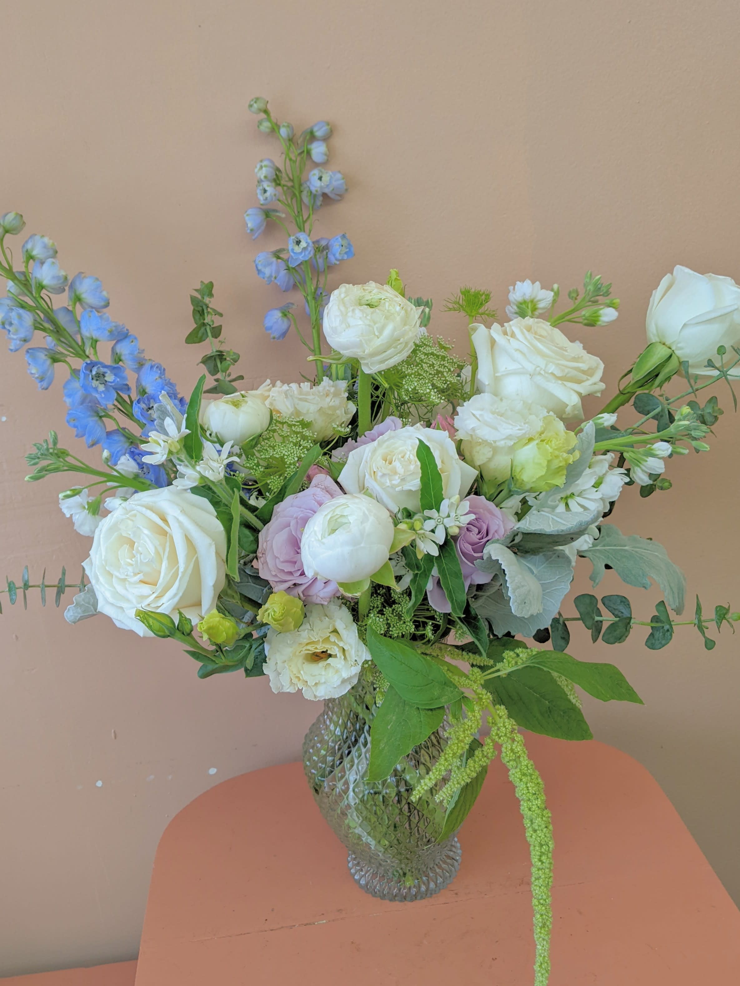Mixed bouquet of white roses, pale blooms, and blue flowers in a glass vase