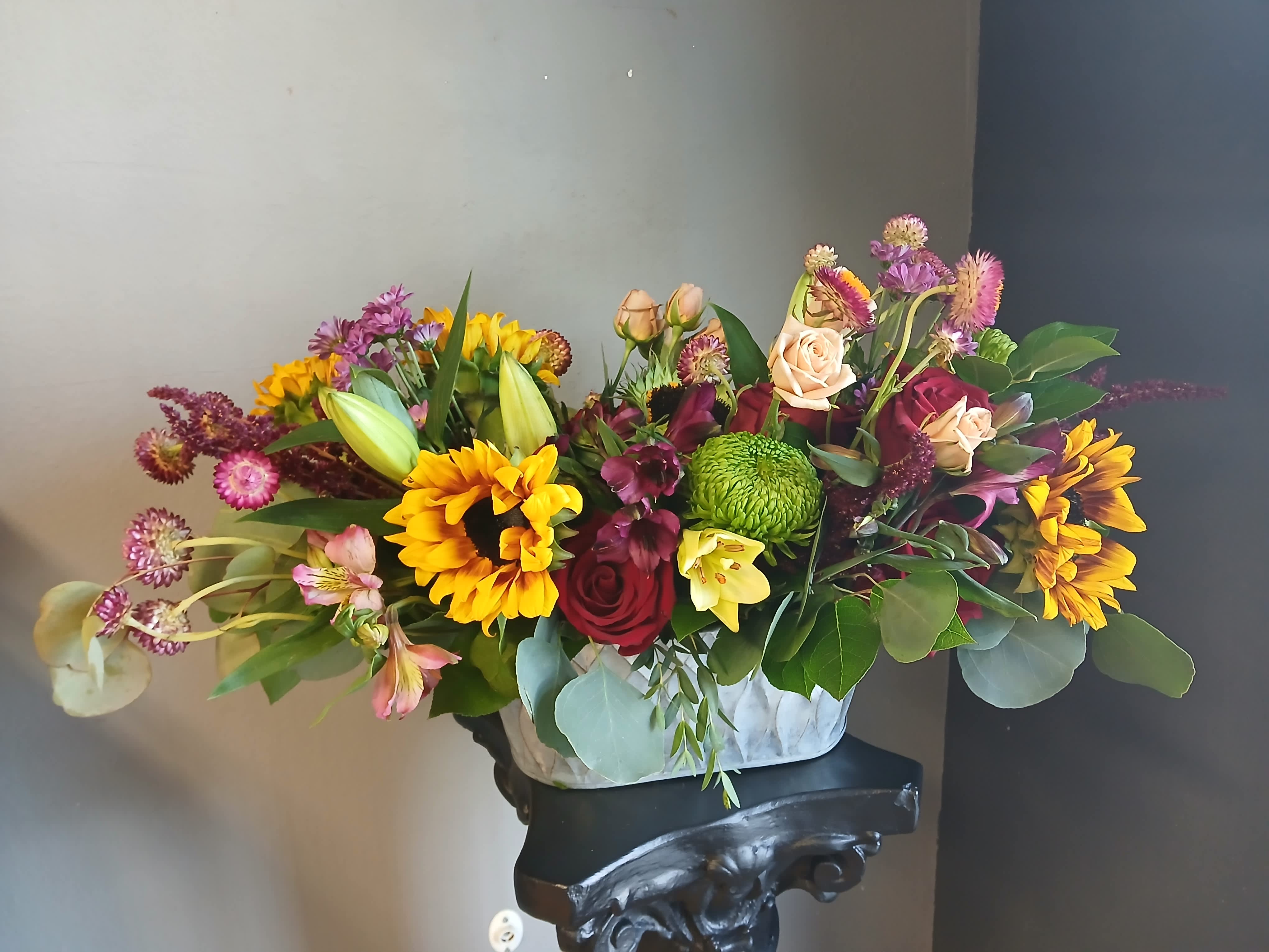 Mixed bouquet of sunflowers, roses, and lilies in a white container