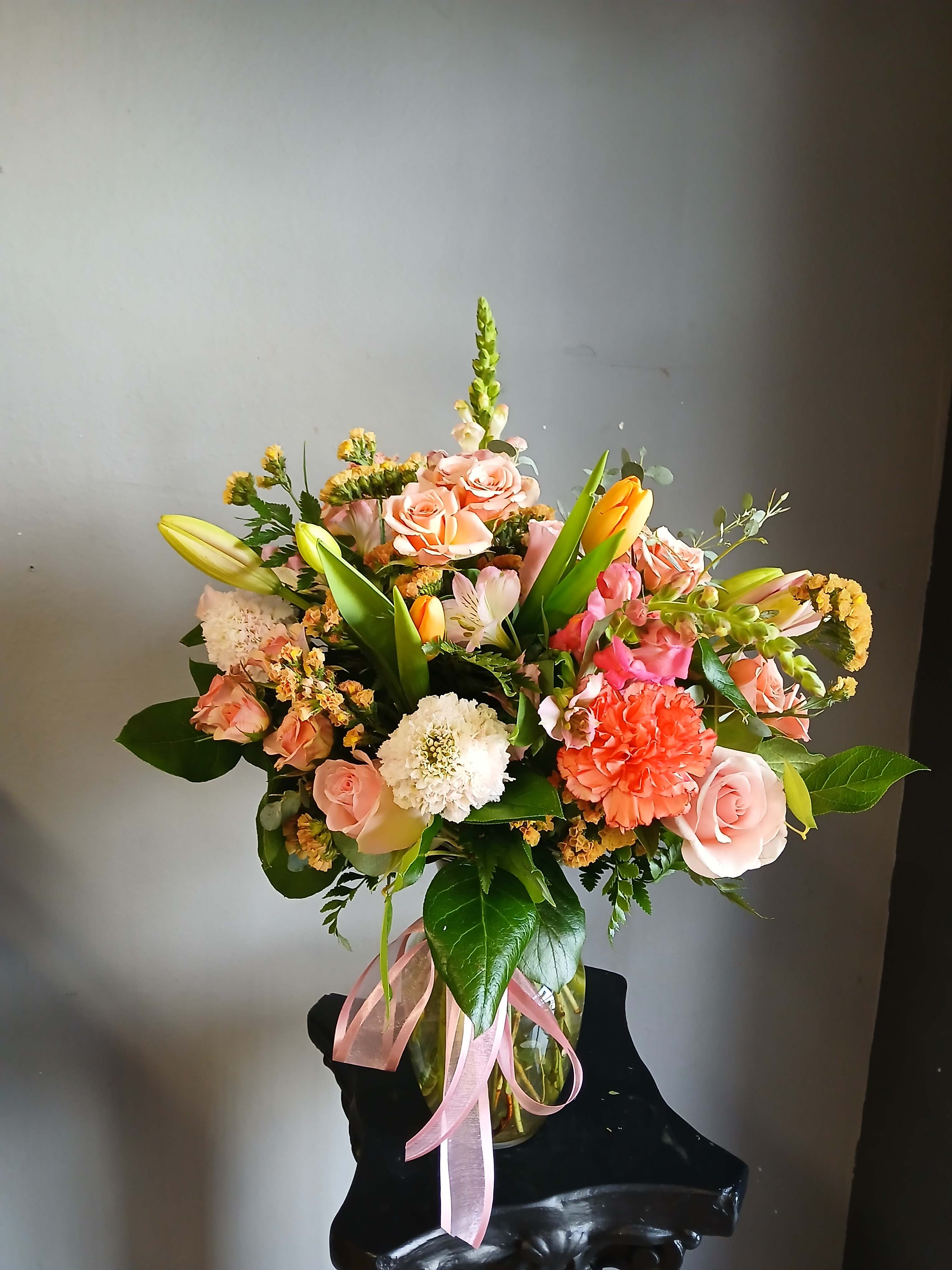 Mixed bouquet of pink roses, lilies, and carnations in a glass vase with a pink ribbon