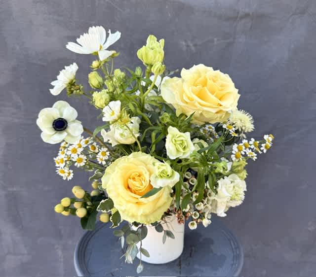 Yellow roses and white flowers arranged in a white vase