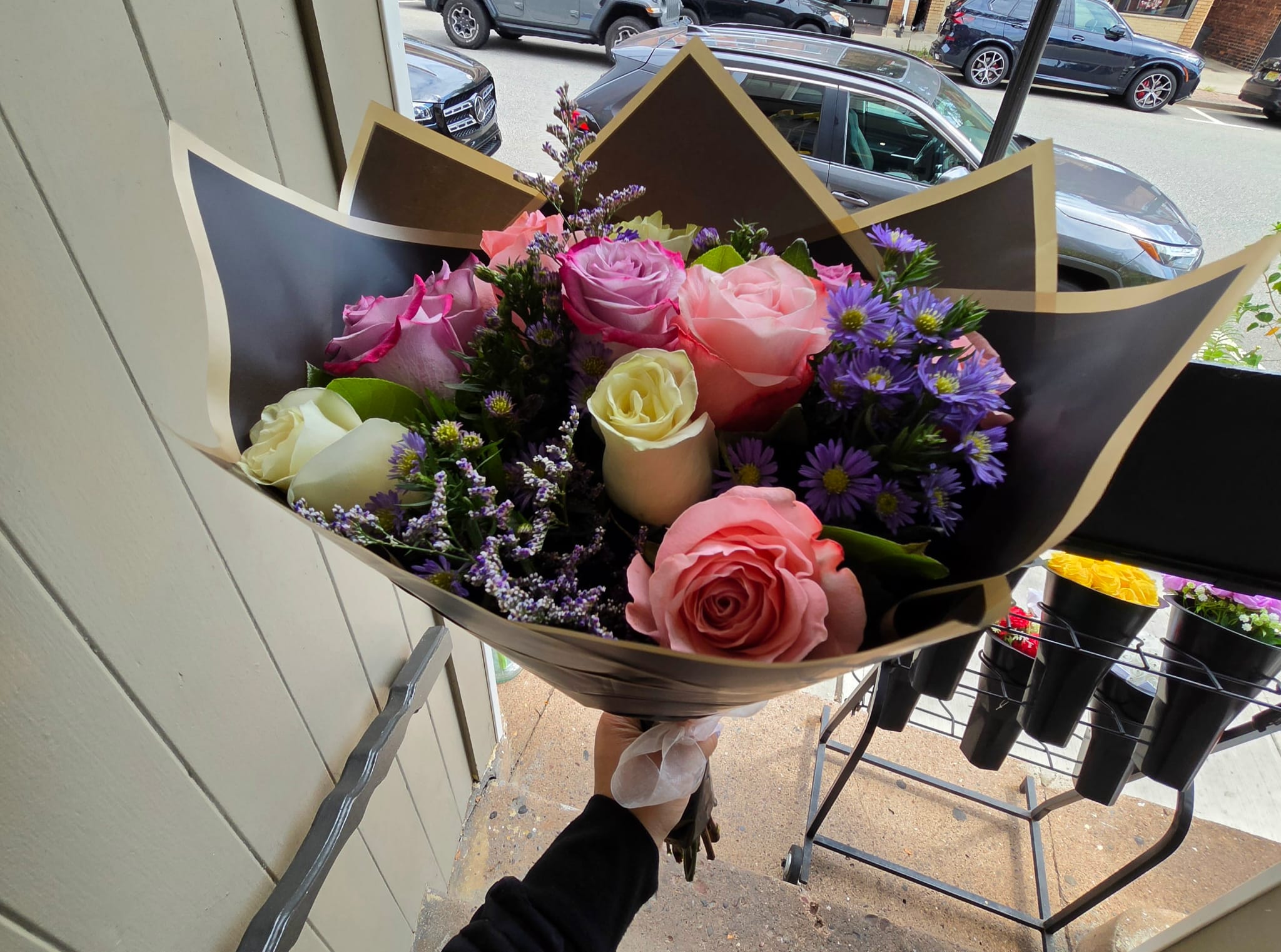 Handheld bouquet of pink, lavender, and white roses with purple filler flowers