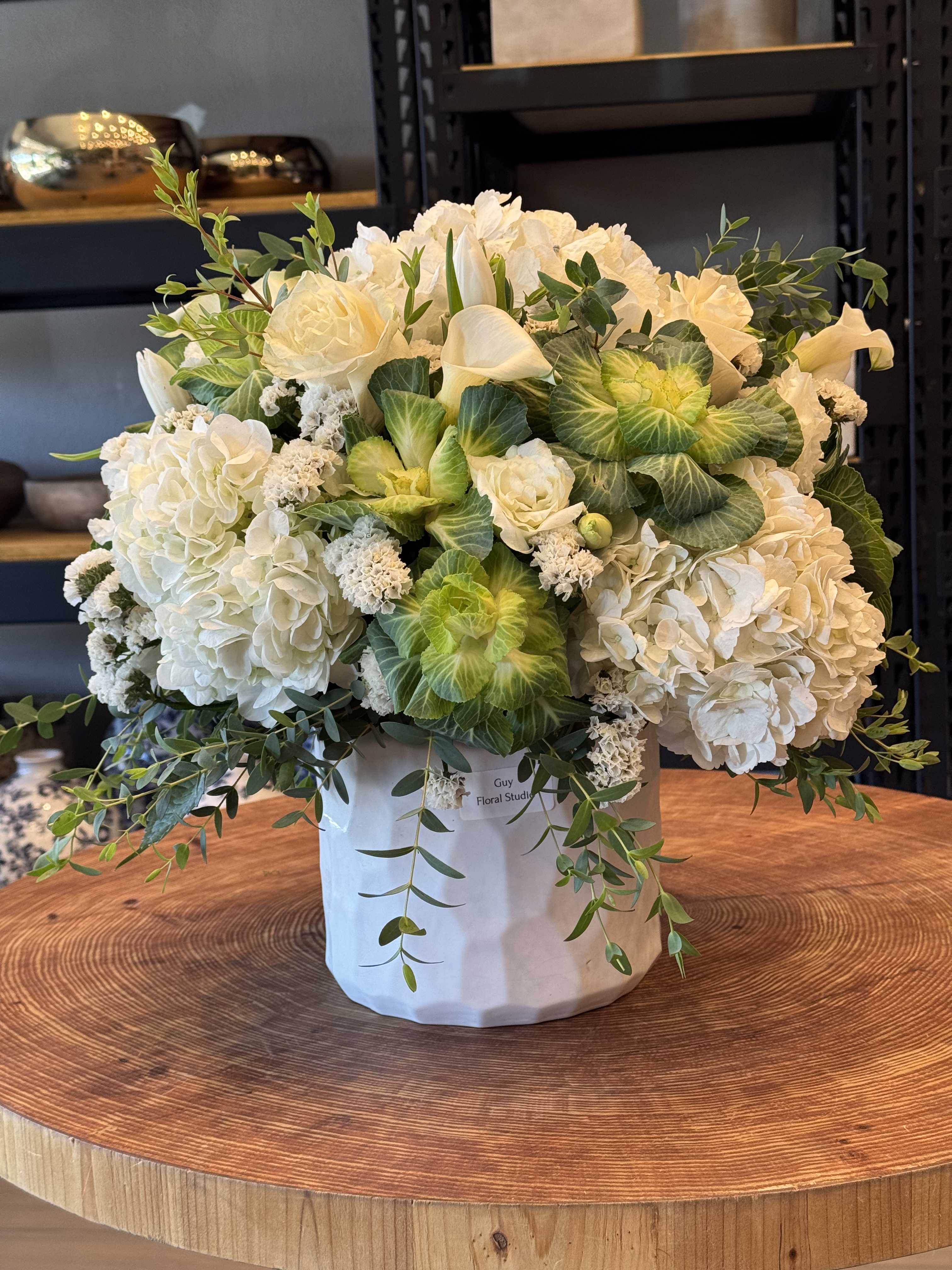 White floral arrangement in a white hatbox with trailing greenery