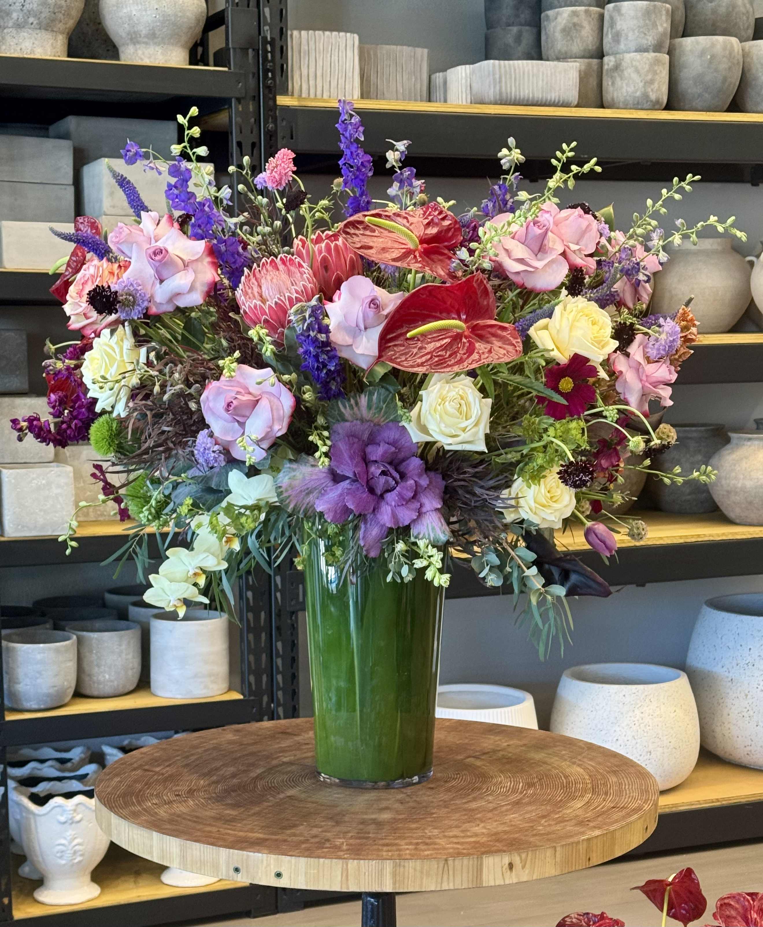 Large mixed bouquet in a tall green vase with pink, purple, red, and yellow blooms