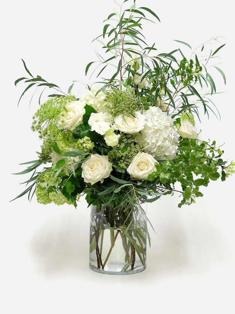 White roses and hydrangeas in a clear glass vase with airy greenery