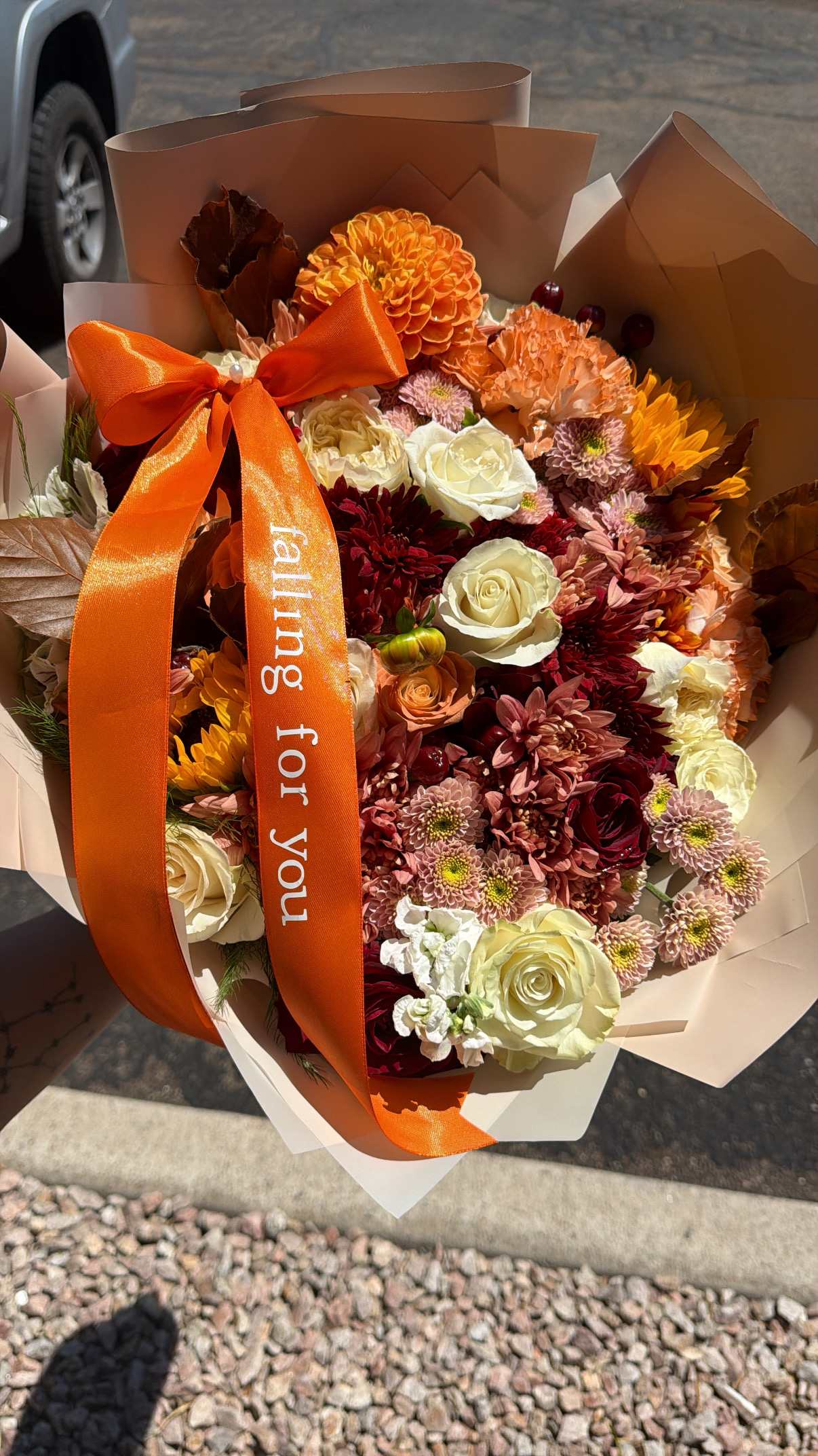 Bouquet of orange, burgundy, and cream flowers with an orange ribbon
