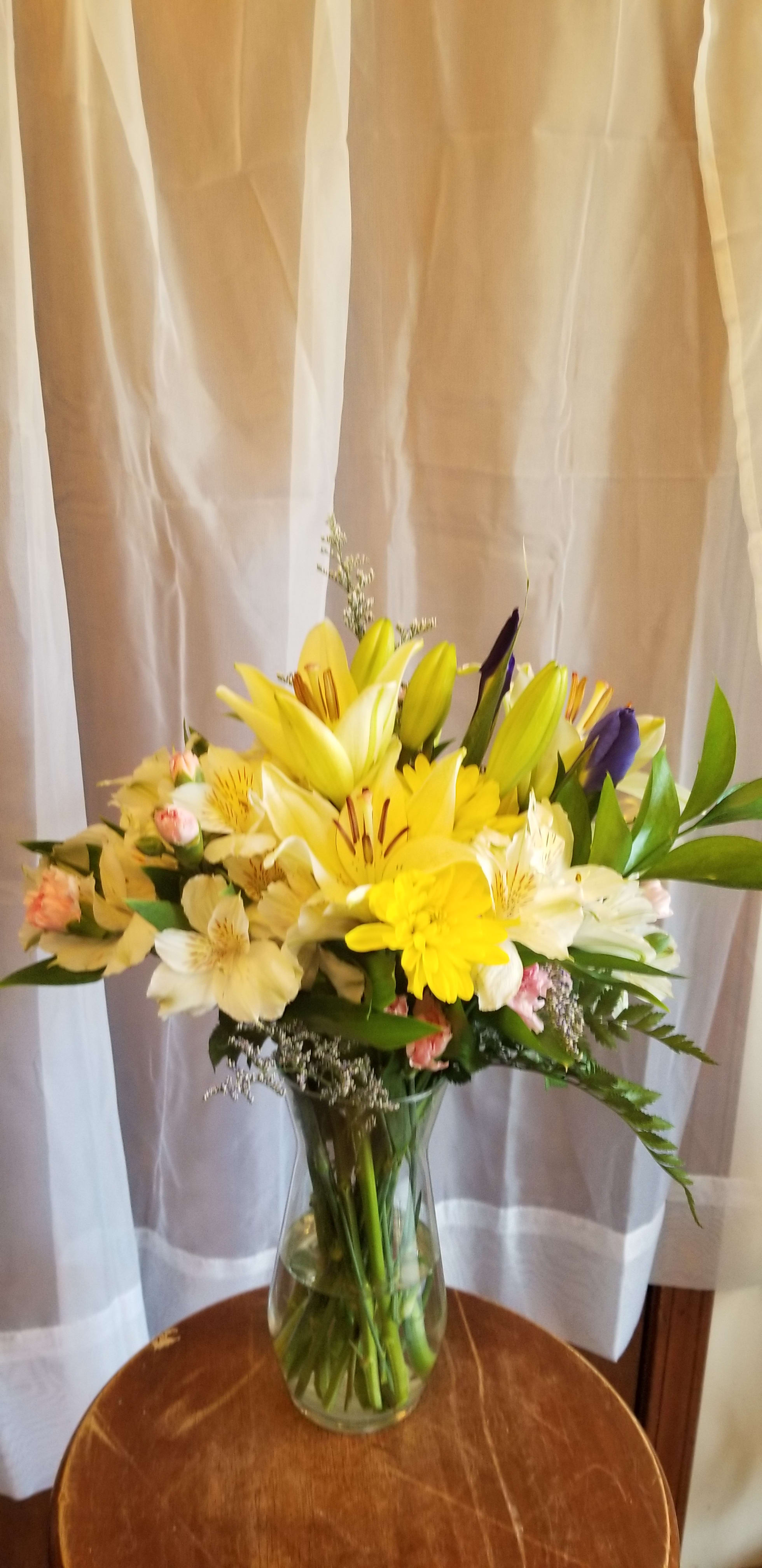 Yellow and white lilies with mixed flowers in a glass vase
