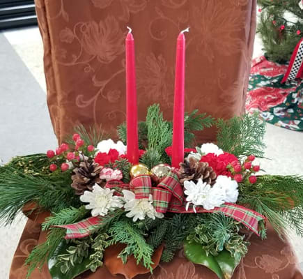 Christmas centerpiece with red candles, white flowers, pinecones, and plaid ribbon