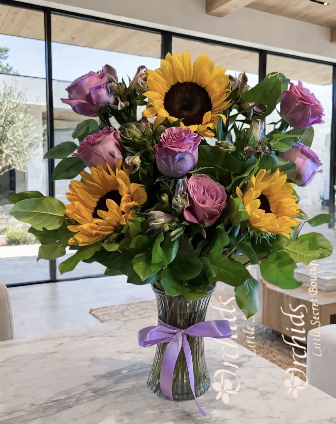 Bouquet of sunflowers and pink roses in a glass vase with a purple ribbon
