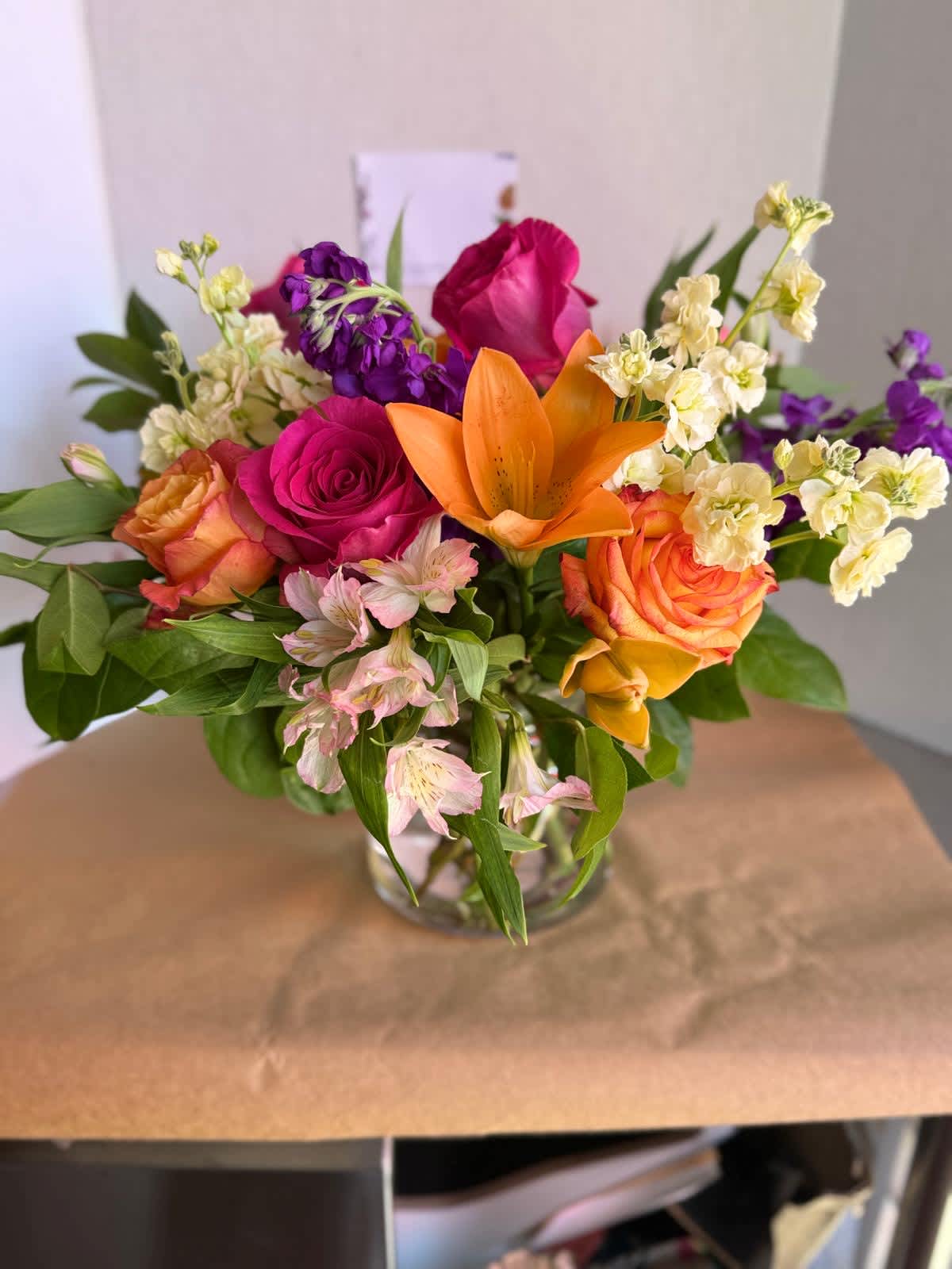 Mixed bouquet of roses, lilies, and purple blooms in a glass vase