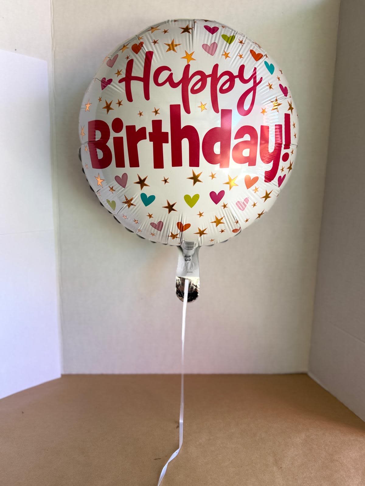 Round foil balloon reading Happy Birthday with heart and star confetti