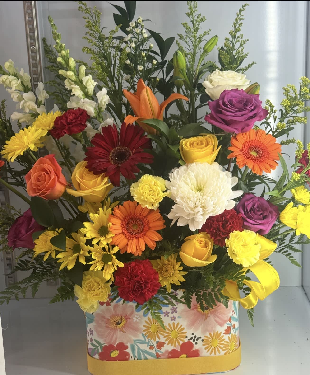 Colorful mixed flower arrangement in a floral-print box with a yellow ribbon