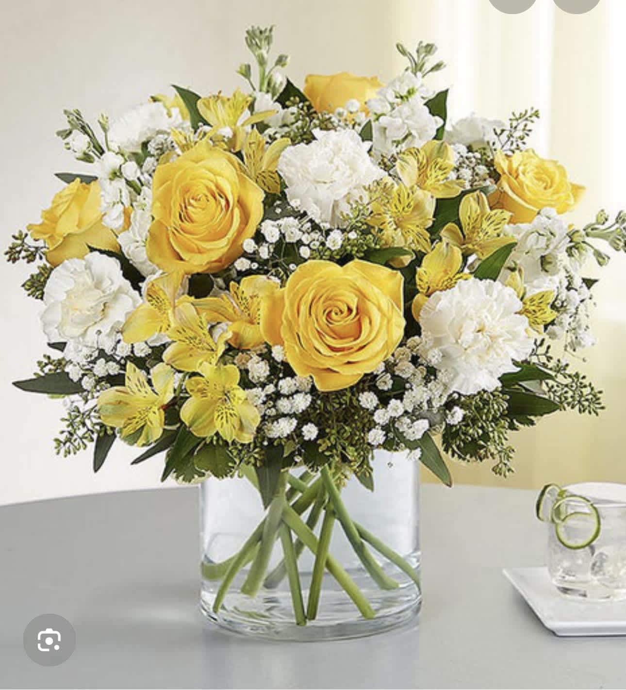 Yellow roses and white flowers arranged in a clear glass vase