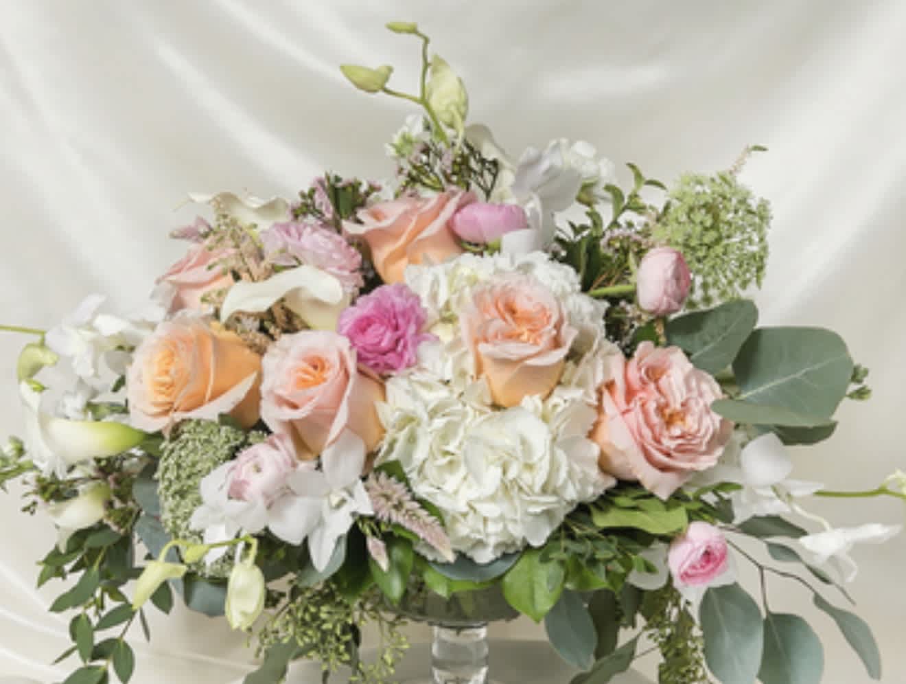 Pastel bouquet of roses, hydrangeas, and white orchids in a glass vase