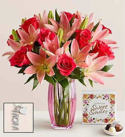 Pink lilies and red roses in a tall glass vase with a card and chocolates