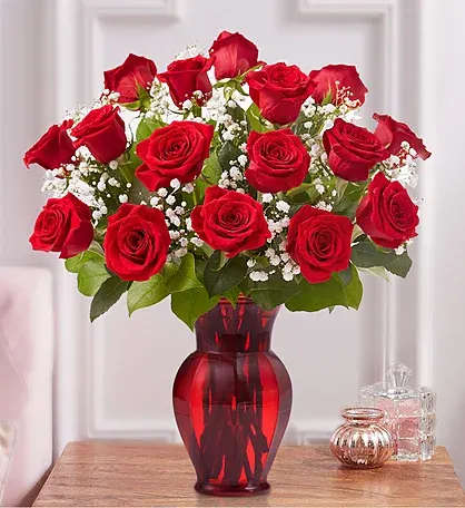 Red roses arranged in a red glass vase with baby's breath